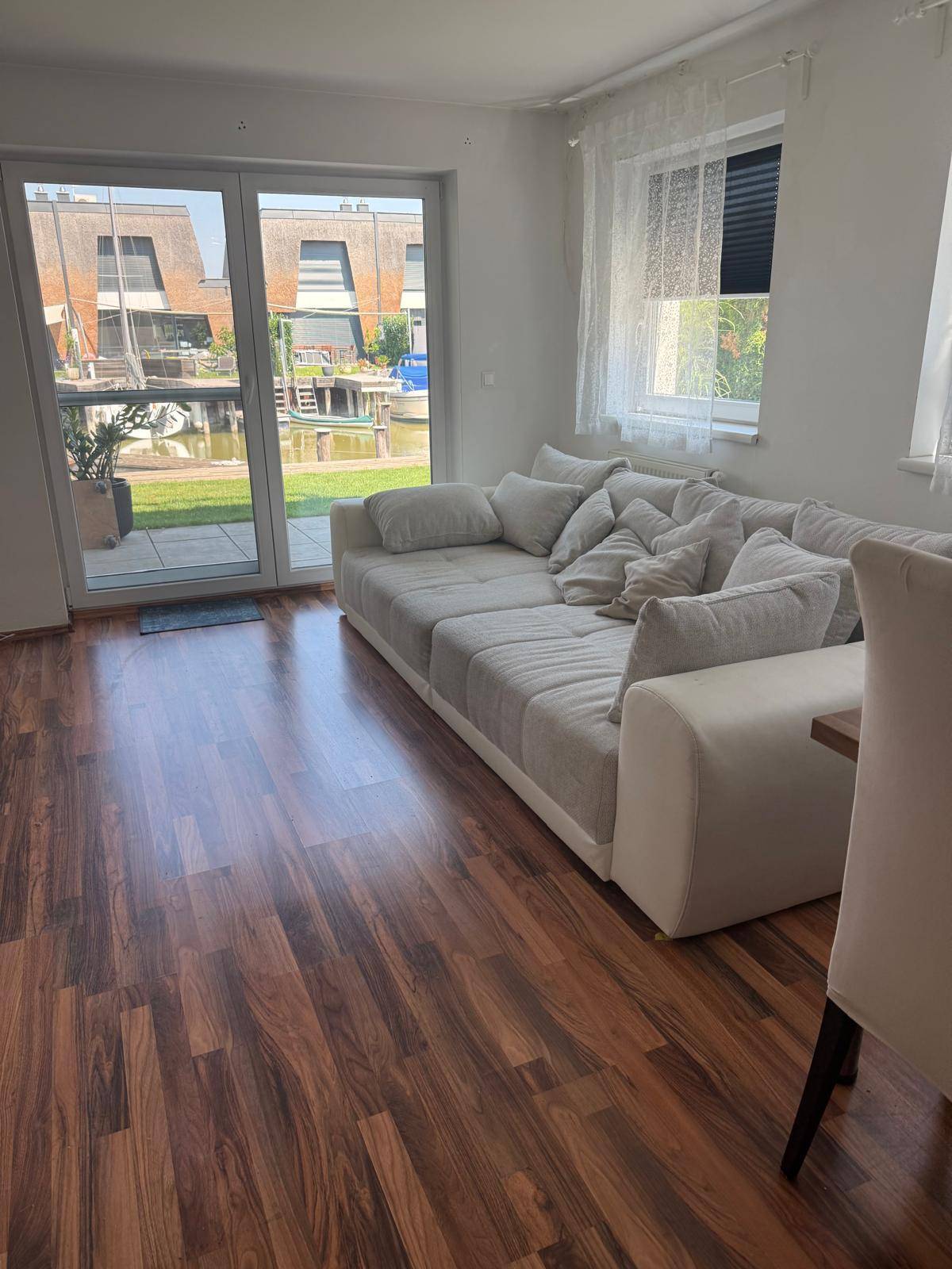 Helles Wohnzimmer mit großem Sofa, Laminatboden und Zugang zur Terrasse.