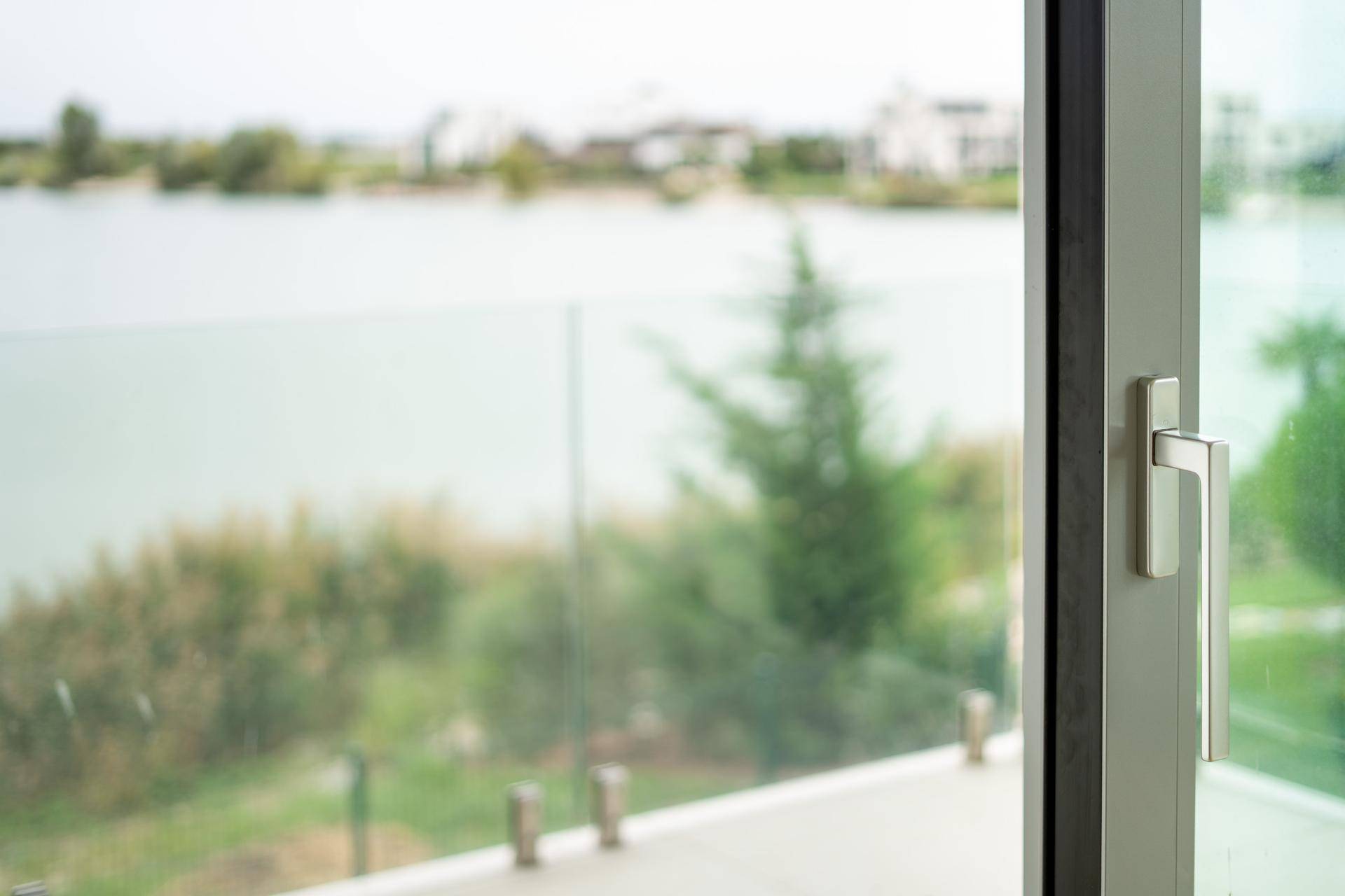 Blick durch ein Fenster auf einen ruhigen See und die umliegende Natur.