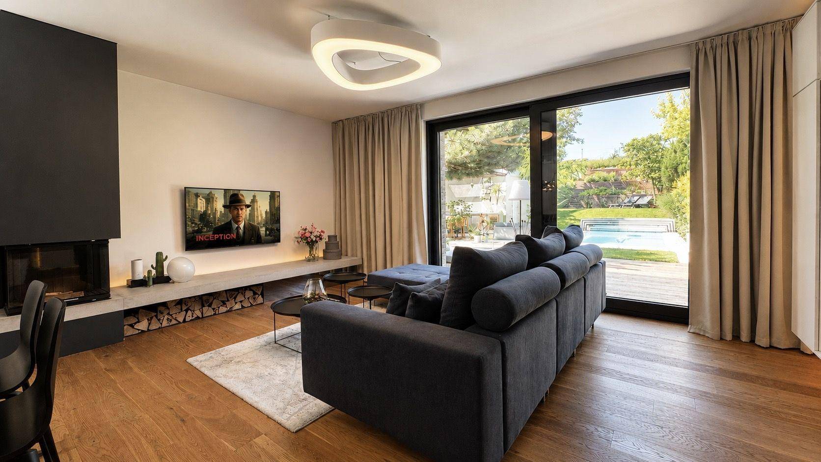 Helles Wohnzimmer mit Kamin, bequemer Couch und großen Fenstern mit Blick auf den Garten und Pool.