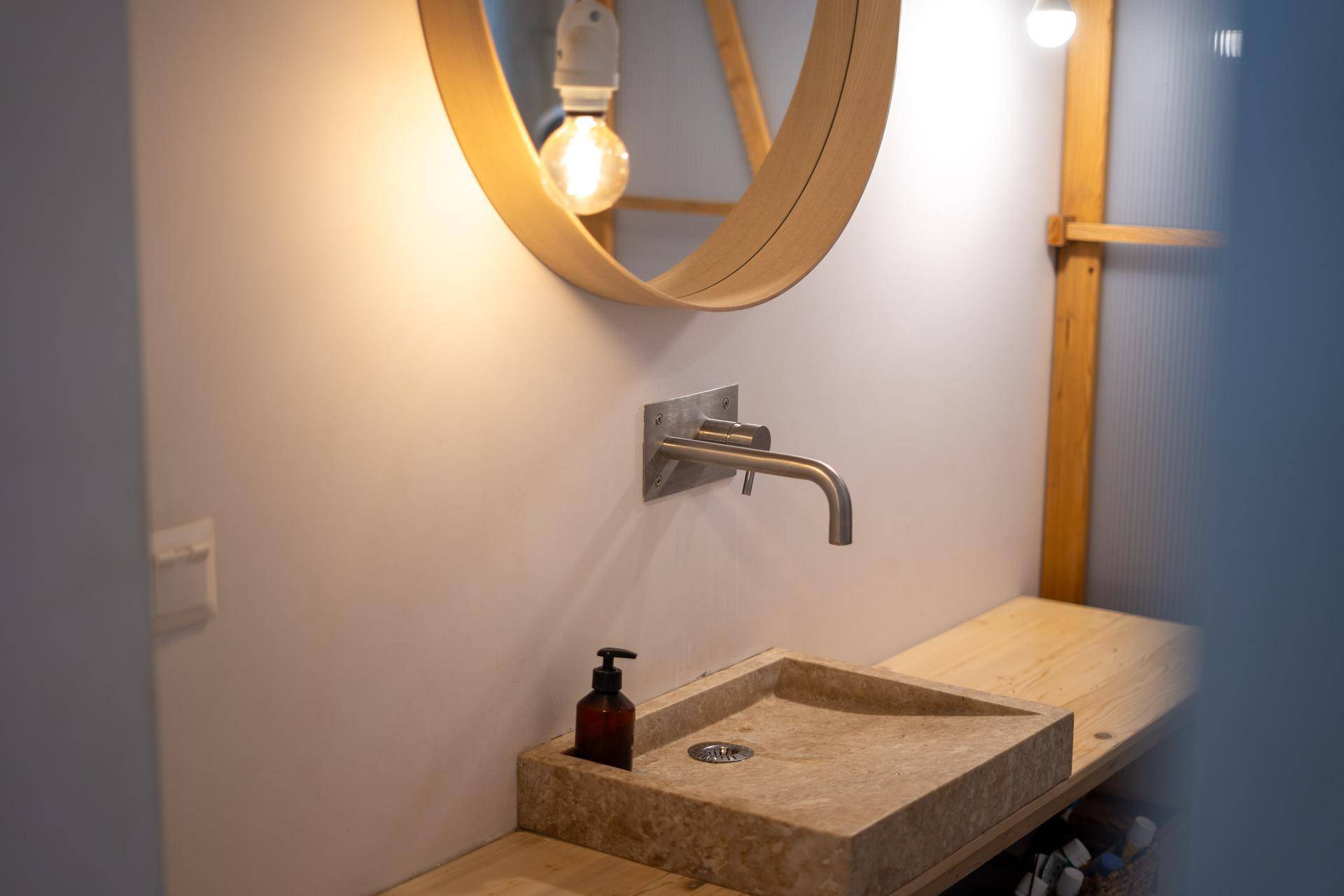 Detailansicht des Natursteinwaschbeckens mit modernem Wasserhahn und rundem Spiegel.