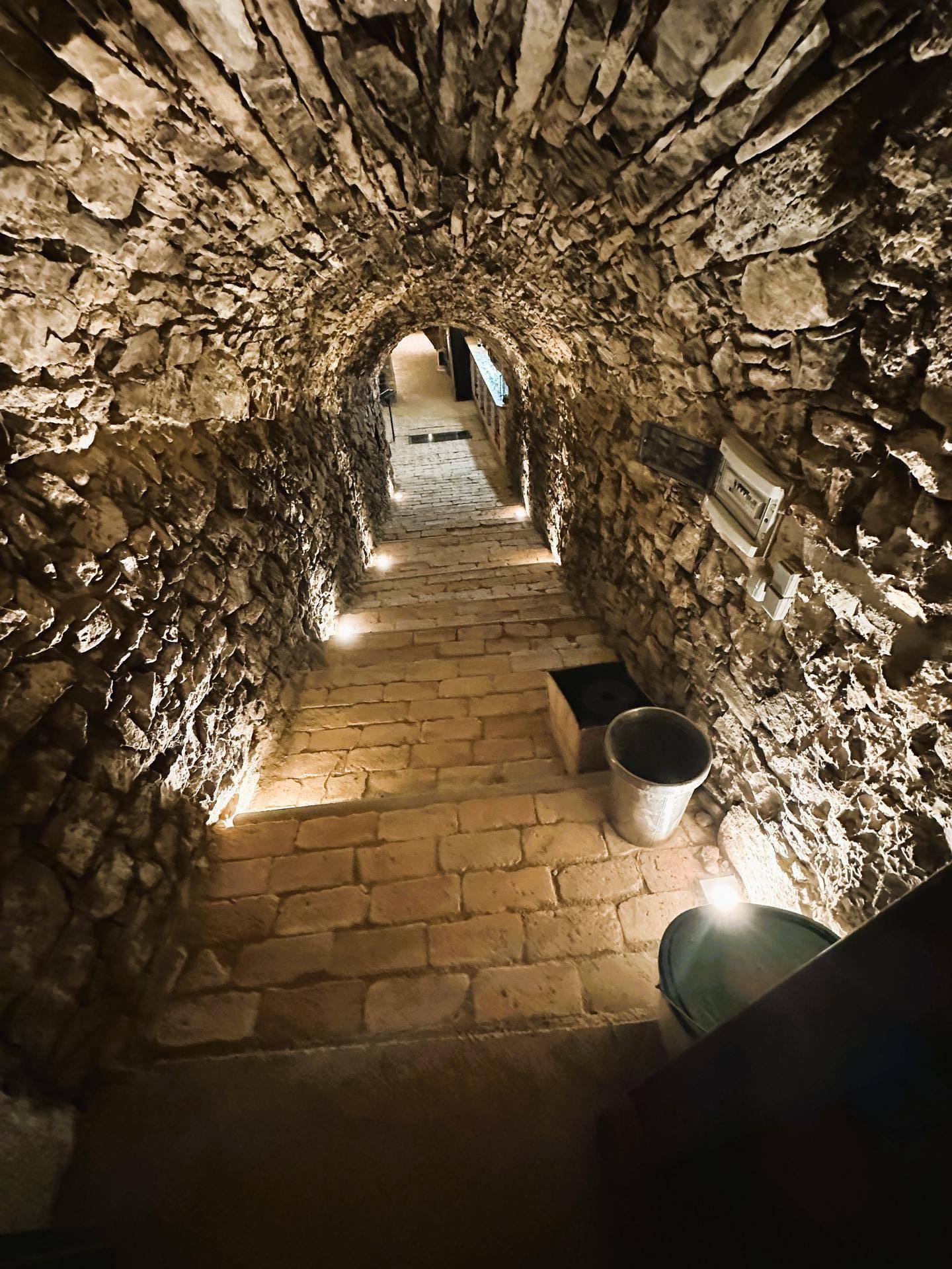 Historischer Steintunnel mit beleuchteter Treppe, der zu einem weiteren Bereich führt.