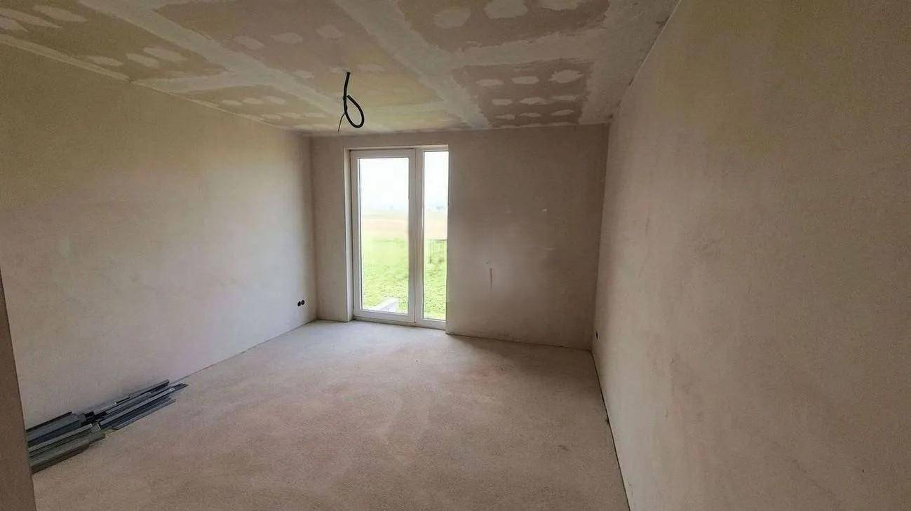 Rohbau-Zimmer mit Tür zum Außenbereich und unfertiger Decke, bereit für den weiteren Ausbau.