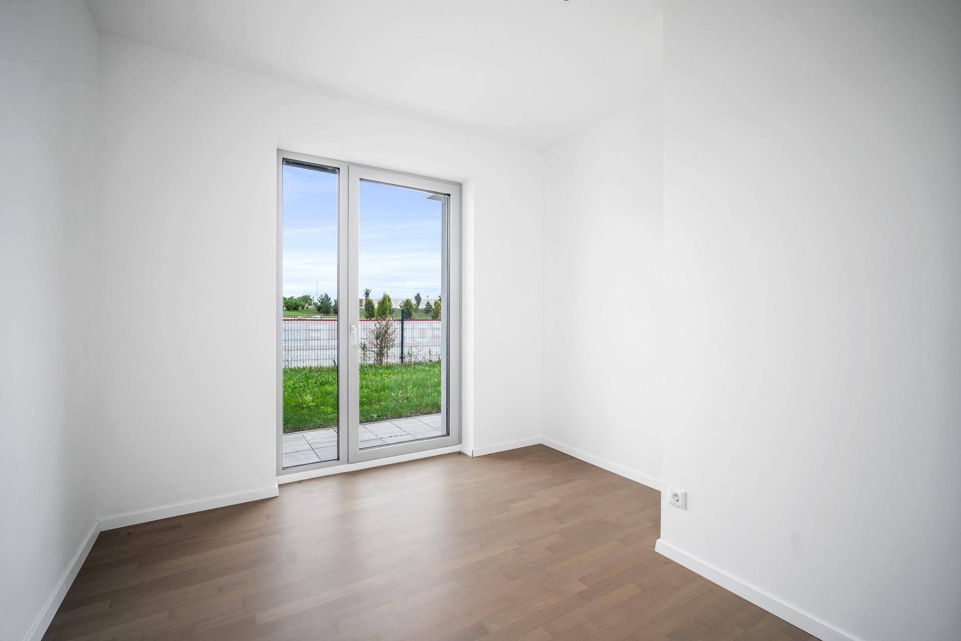 Helles Zimmer mit Parkettboden und direktem Zugang zu einer kleinen Grünfläche.