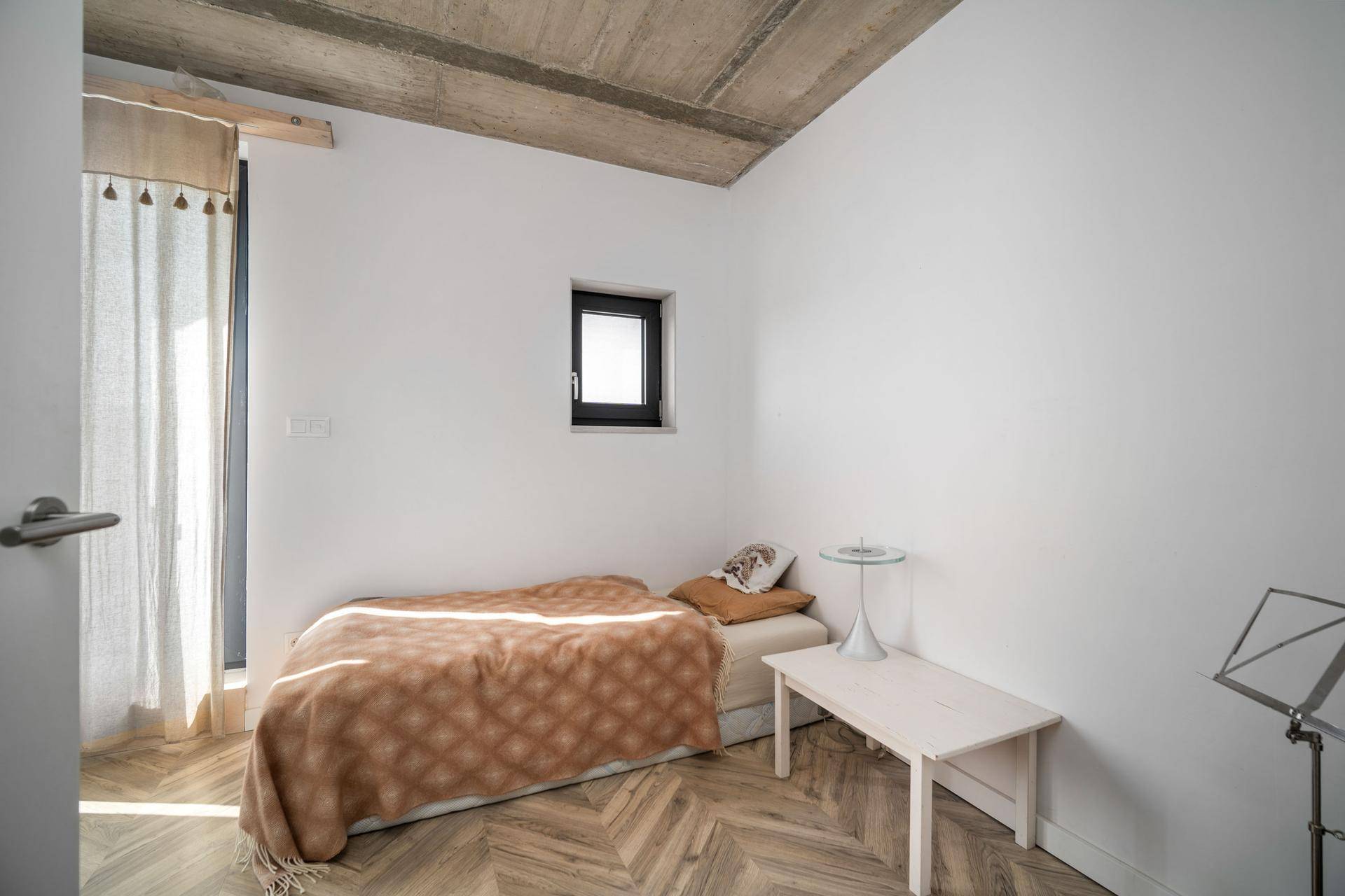 Gemütliches Schlafzimmer mit Einzelbett, Parkettboden und kleinem Fenster.