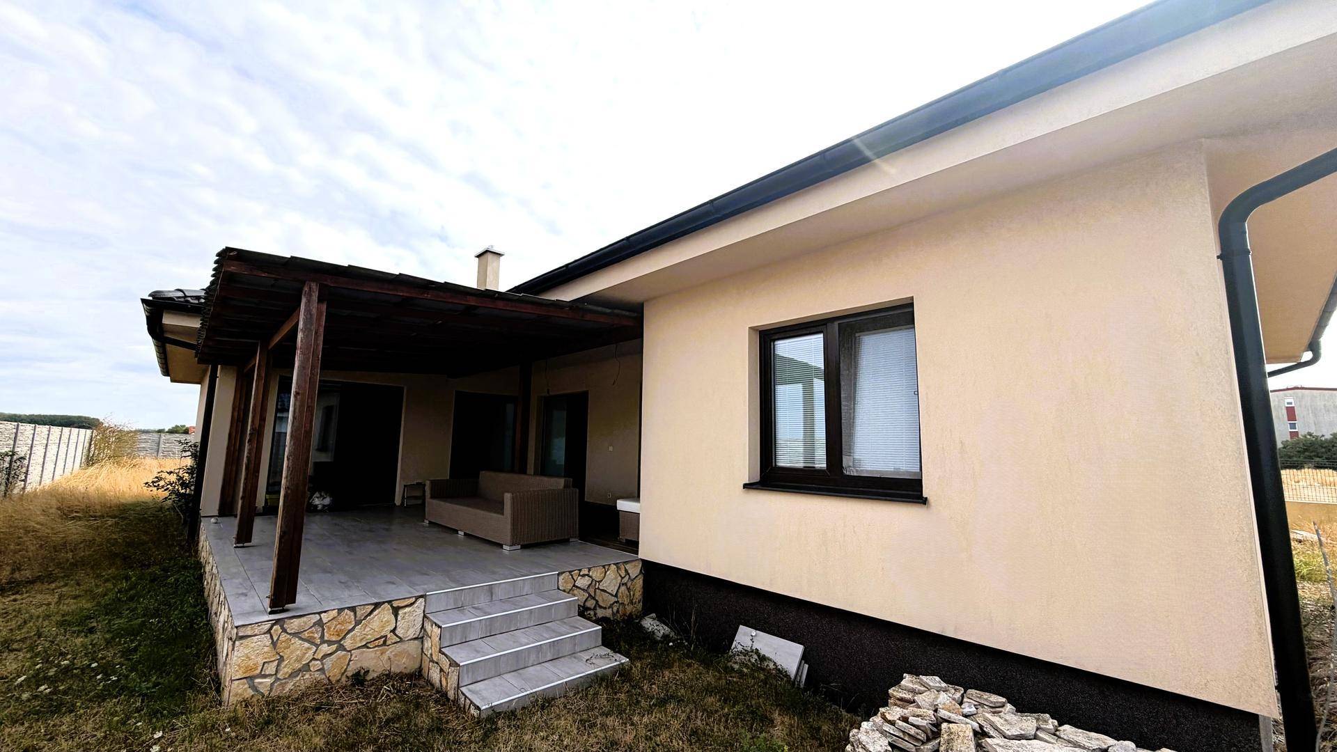 Seitenansicht des Hauses mit überdachter Terrasse und Zugang zum Garten.