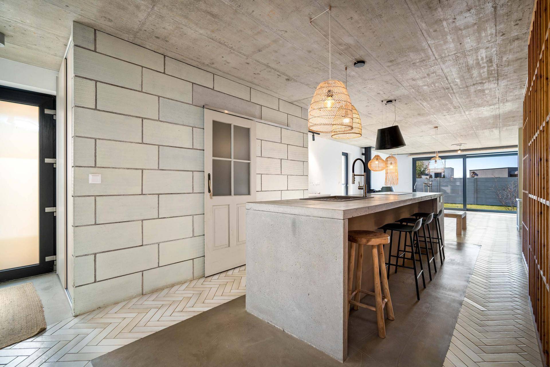Offener Küchenbereich mit Betoninsel, Holzelementen und Zugang zum Garten.
