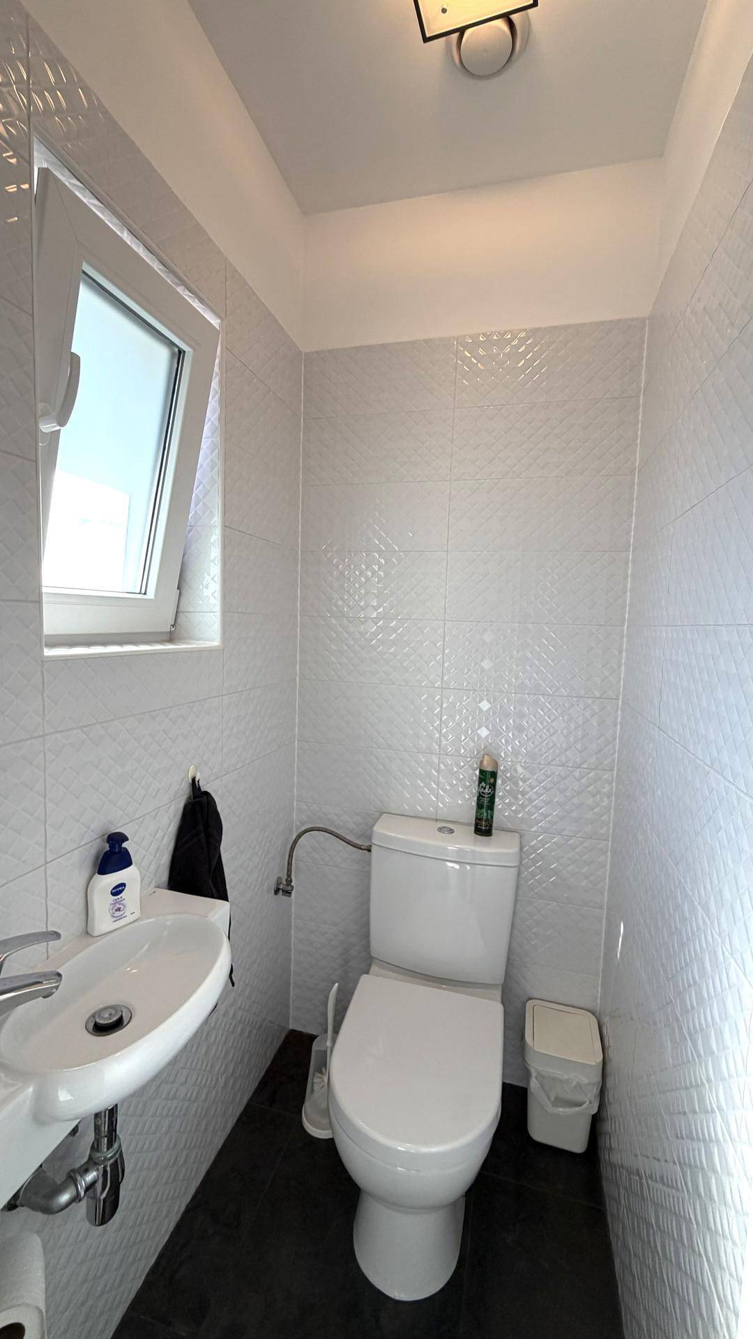 Kleines Gäste-WC mit Fenster, Waschbecken und modernen Fliesen.