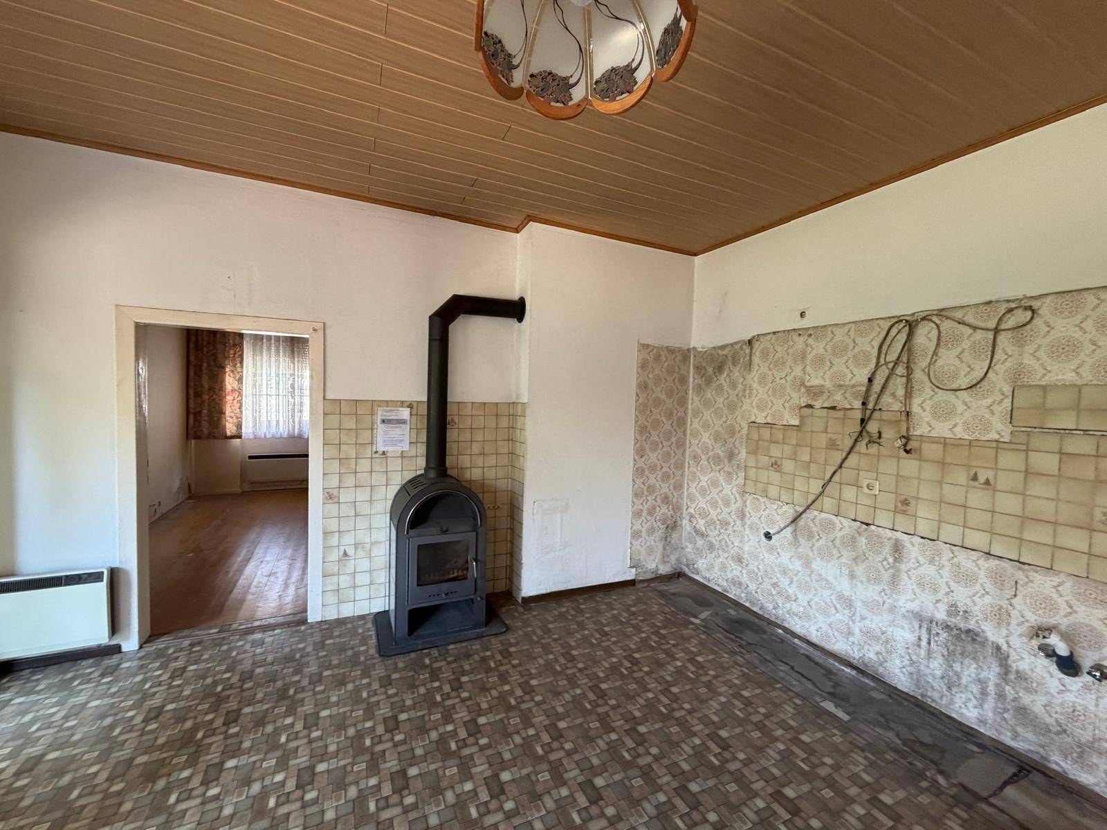 Ehemalige Küche mit Holzofen, Fliesenresten an der Wand und Holzdecke.