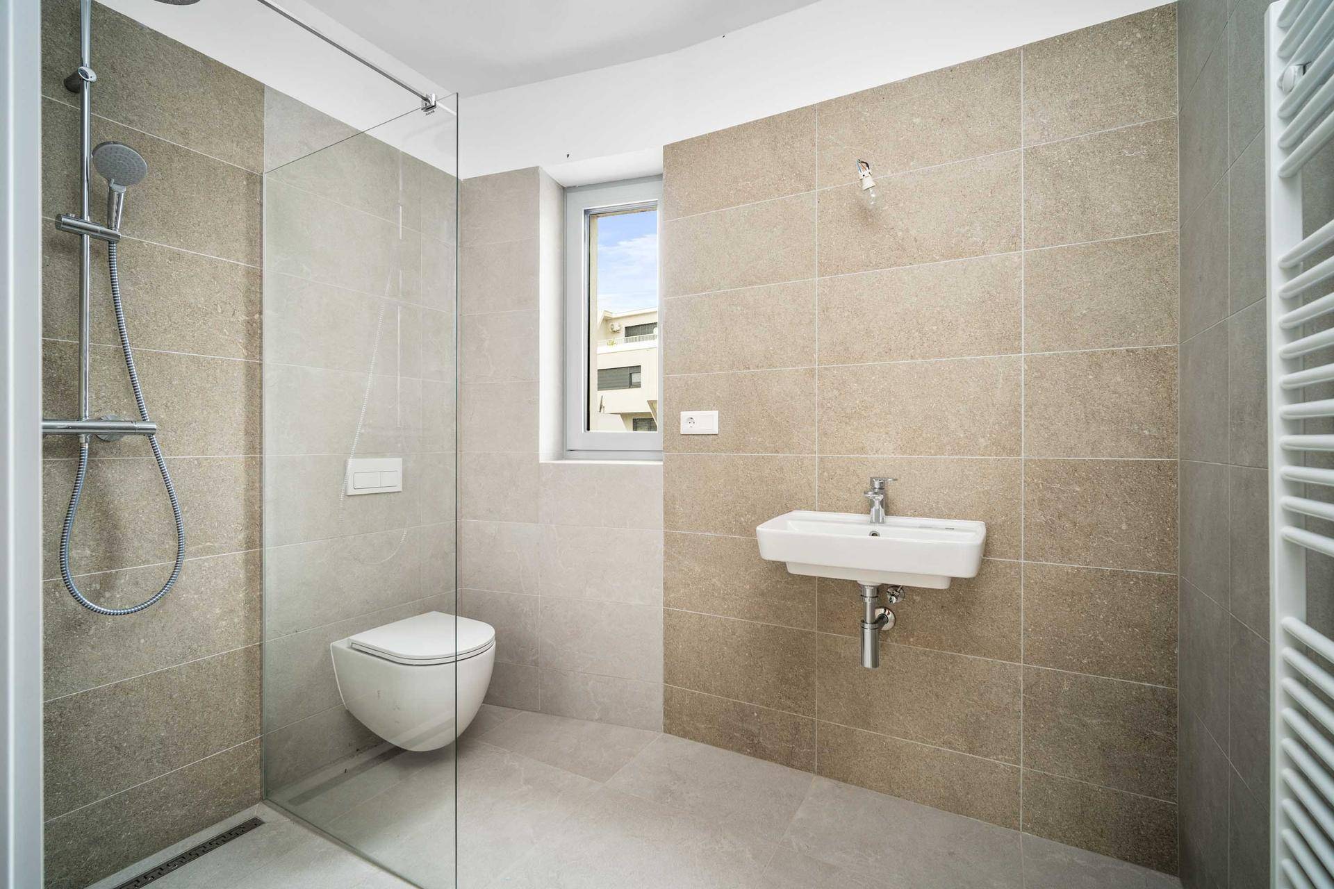 Modernes Badezimmer mit begehbarer Dusche, Wand-WC und Waschbecken in neutralen Farbtönen.