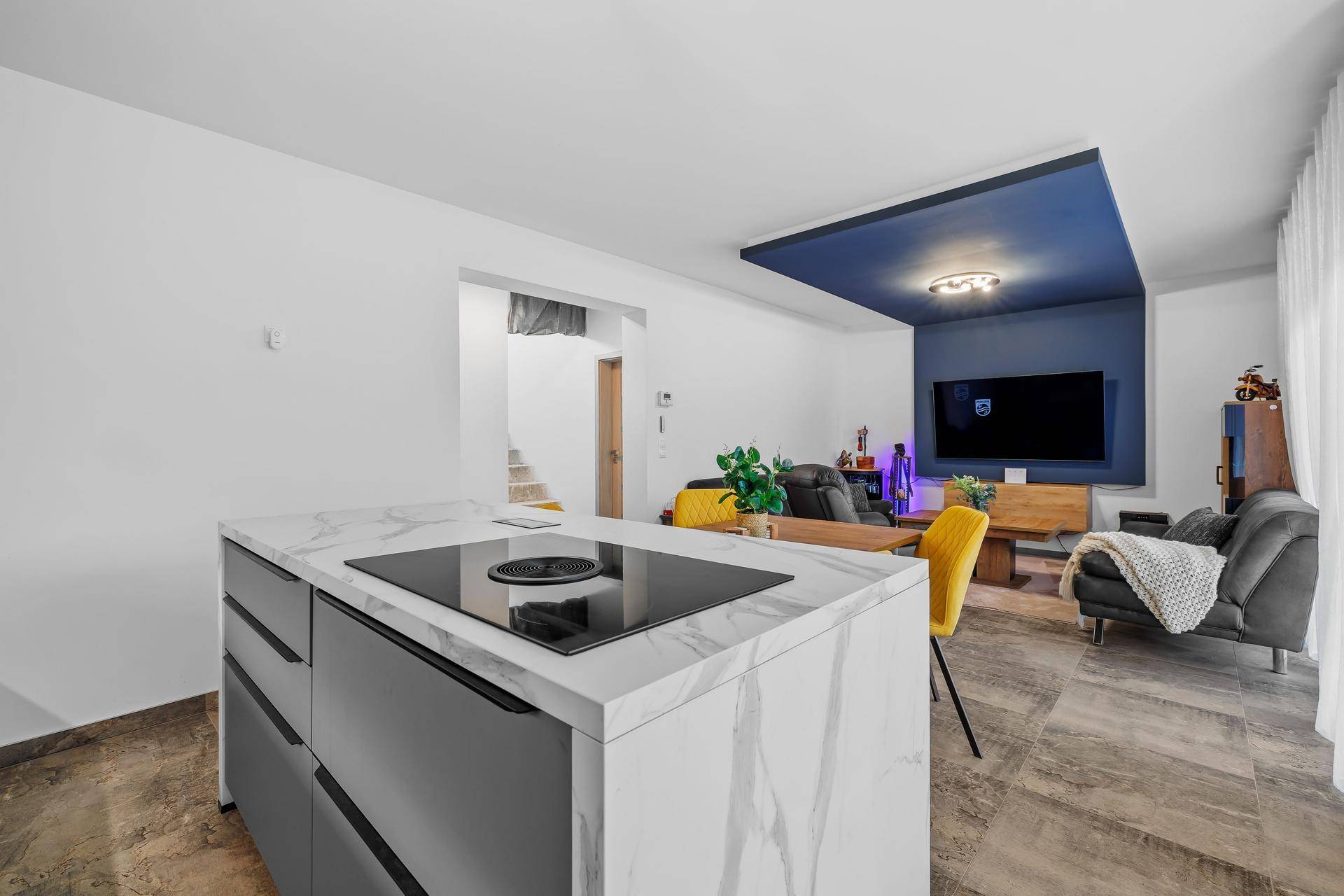 Offener Wohnbereich mit Kücheninsel, integriertem Kochfeld und Blick auf den Wohnbereich.