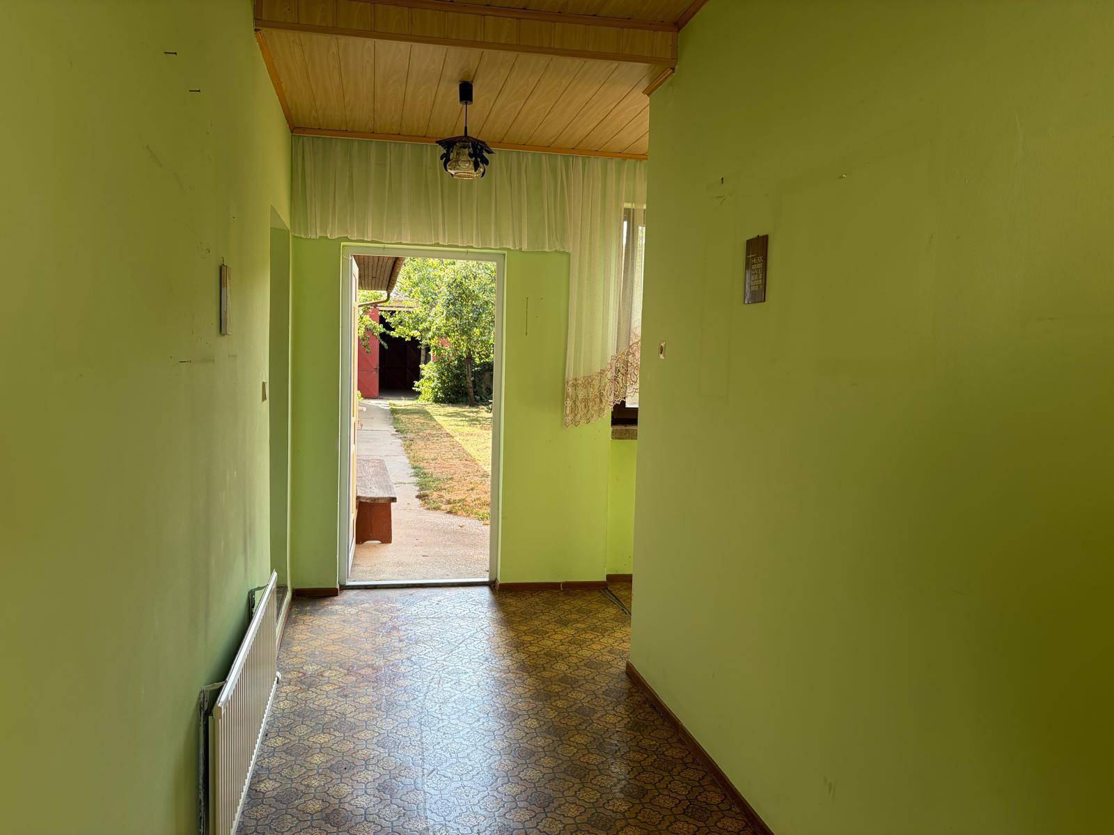 Flur mit grün gestrichenen Wänden, gemustertem Linoleumboden und Holzbalkendecke.