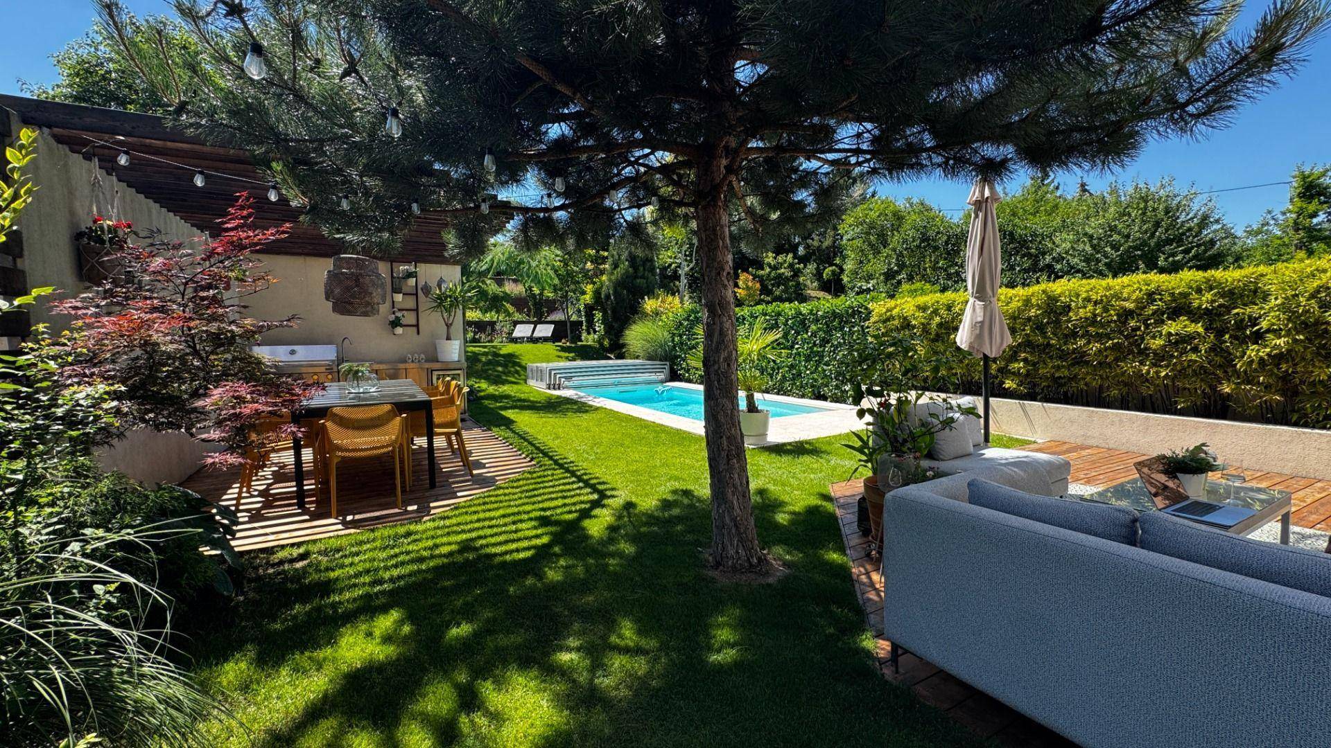 Weitläufiger Garten mit gepflegtem Rasen, schattenspendenden Bäumen, Pool und verschiedenen Sitzbereichen.