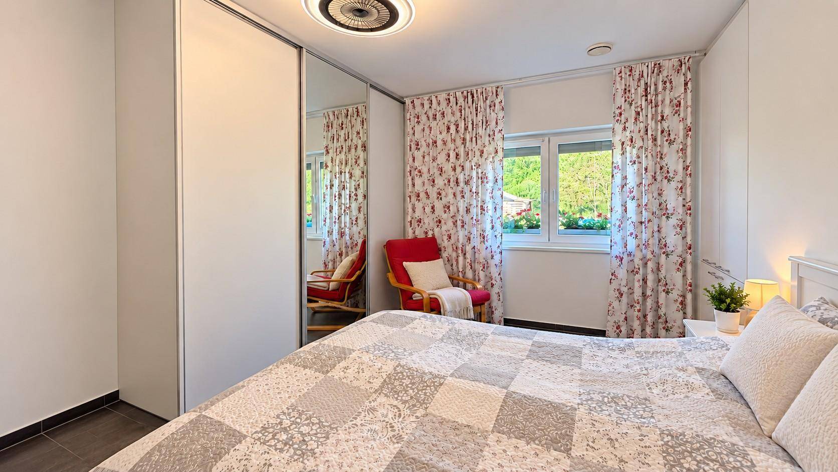 Gemütliches Schlafzimmer mit Doppelbett, Spiegelschrank und floralen Vorhängen.