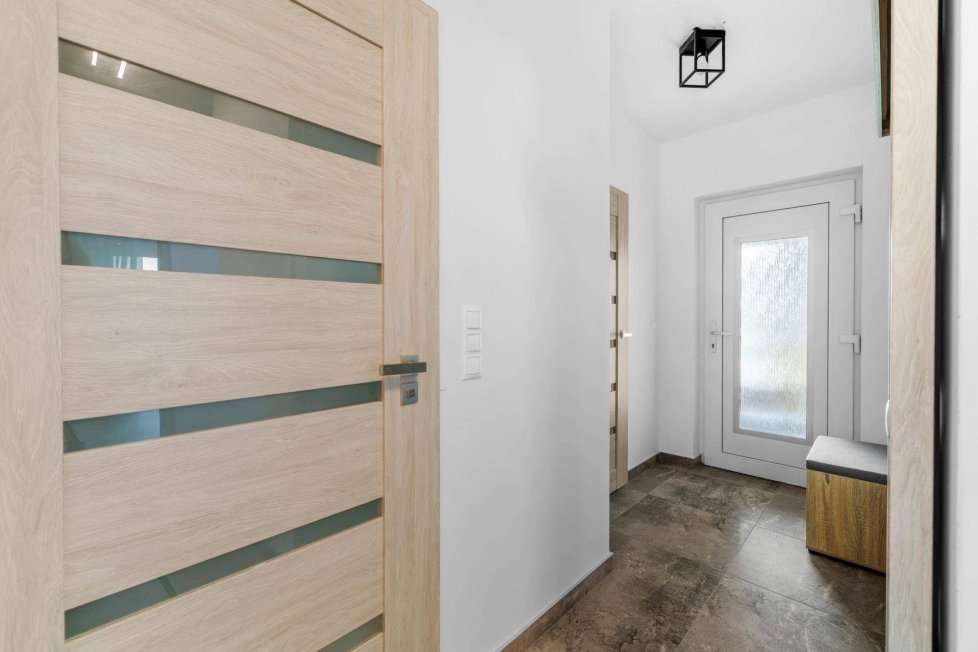 Heller Eingangsbereich mit moderner Holztür und Fliesenboden, der zu den Wohnräumen führt.