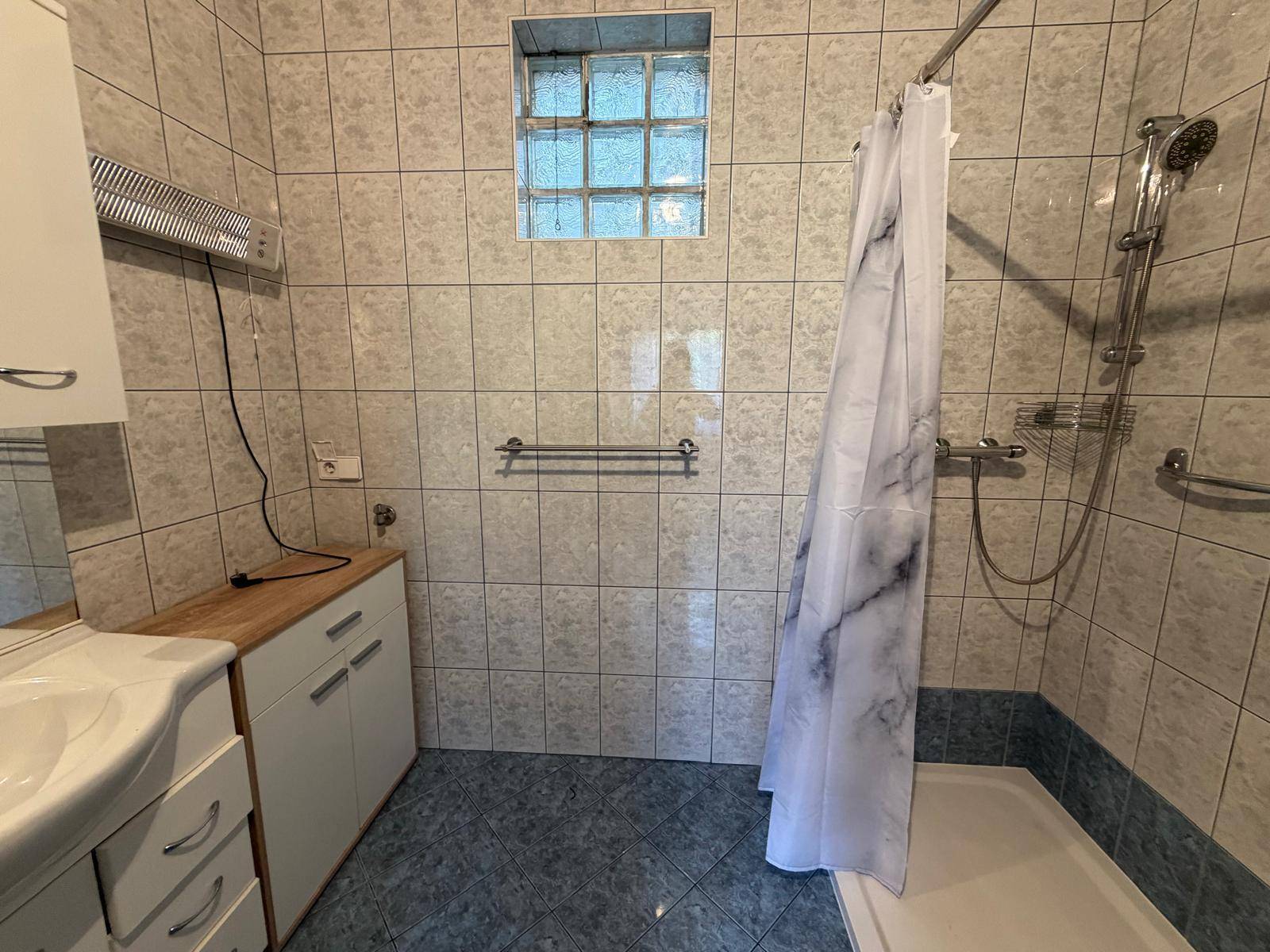 Badezimmer mit Duschkabine, Fliesenboden und Glasbausteinfenster.