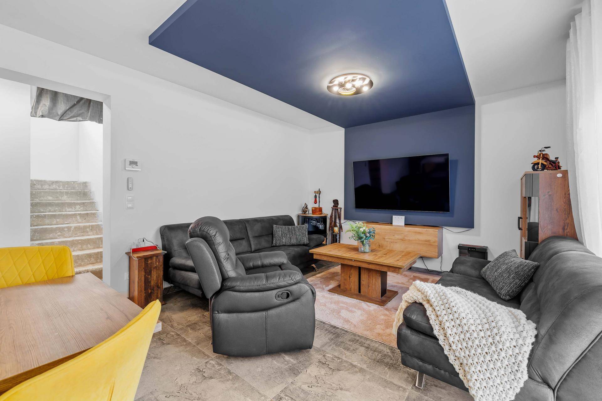 Gemütlicher Wohnbereich mit bequemen Sofas, Fernseher und dekorativer Deckenbeleuchtung.