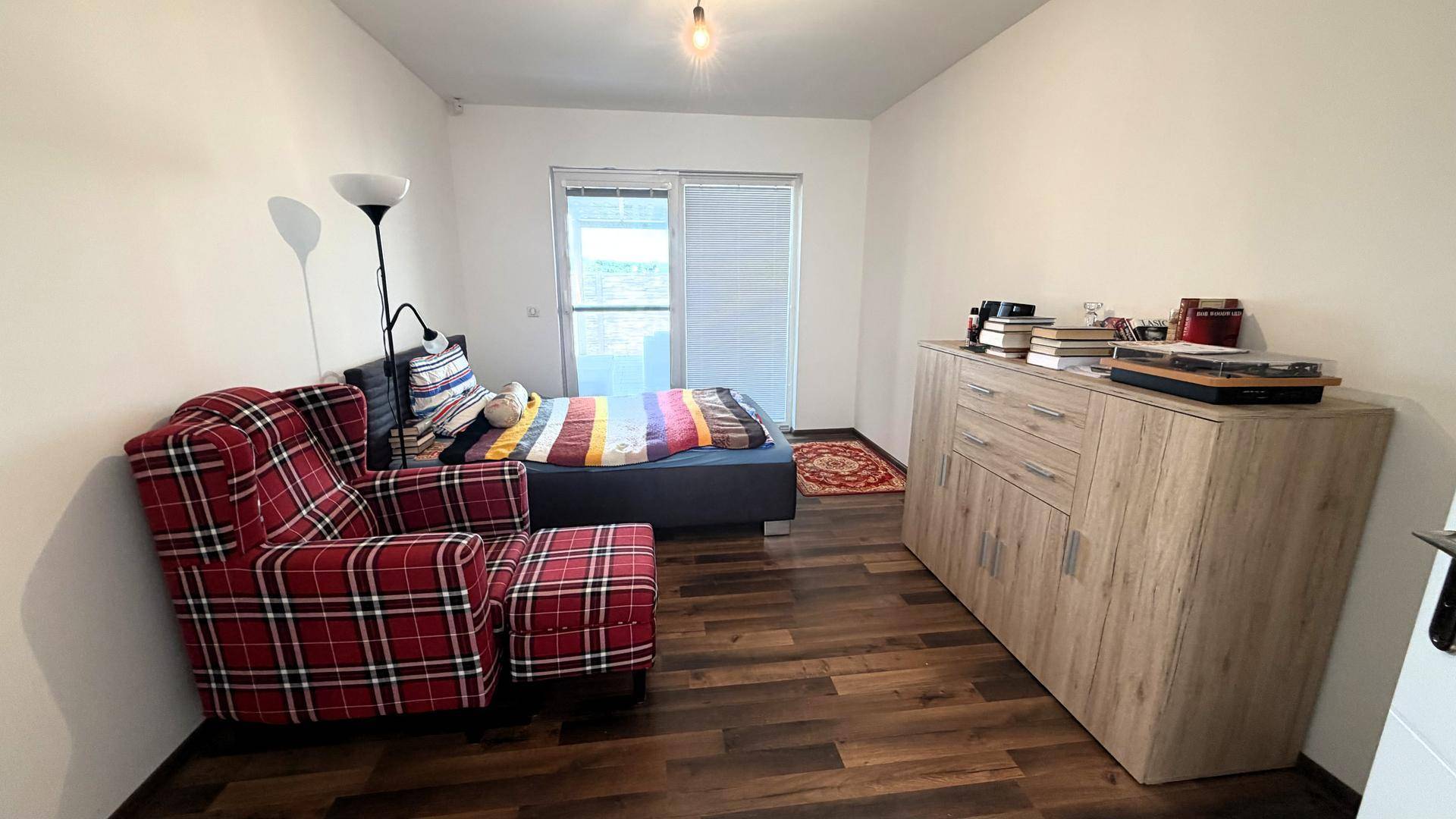 Schlafzimmer mit kariertem Sessel, Bett und Kommode.
