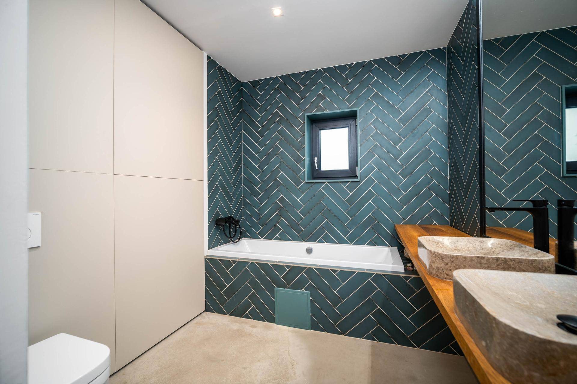Modernes Badezimmer mit Badewanne, Doppelwaschbecken und blauen Fischgrätfliesen.