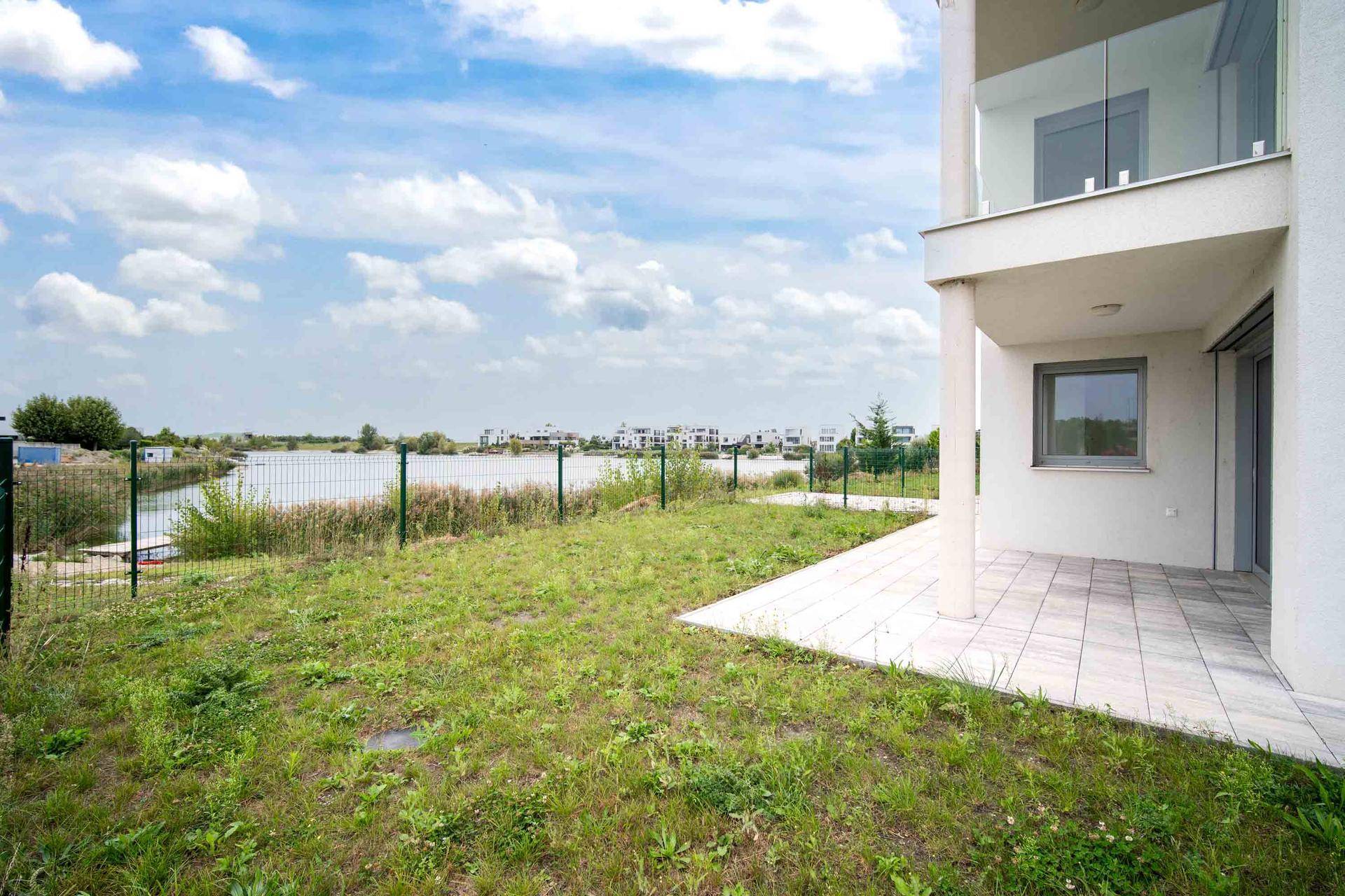Gartenbereich mit gepflasterter Terrasse und direktem Blick auf den angrenzenden See.
