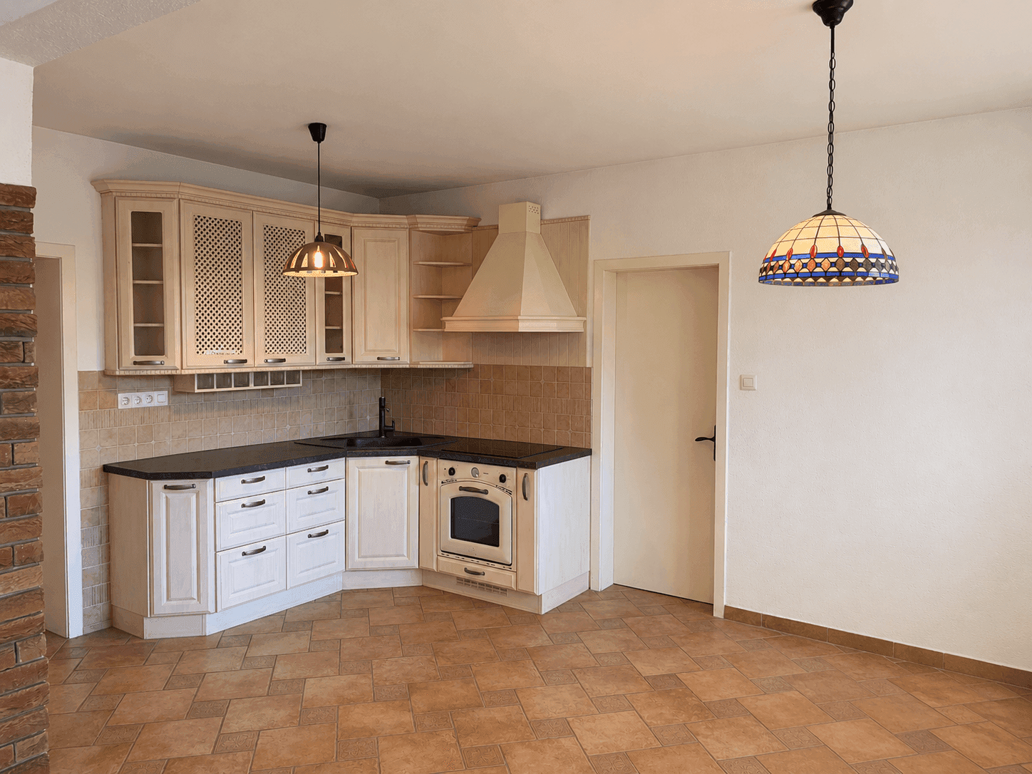 Traditionelle Einbauküche mit hellen Schränken, dunkler Arbeitsplatte, Backofen und Dunstabzugshaube.