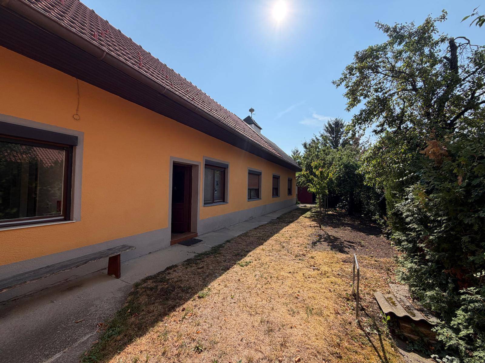 Seitenansicht des Hauses mit Eingang und Gartenbereich unter strahlendem Sonnenschein.