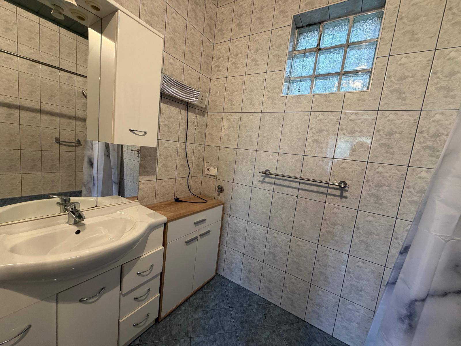 Badezimmer mit Waschbecken, Spiegelschrank und Duschbereich mit Fliesen.