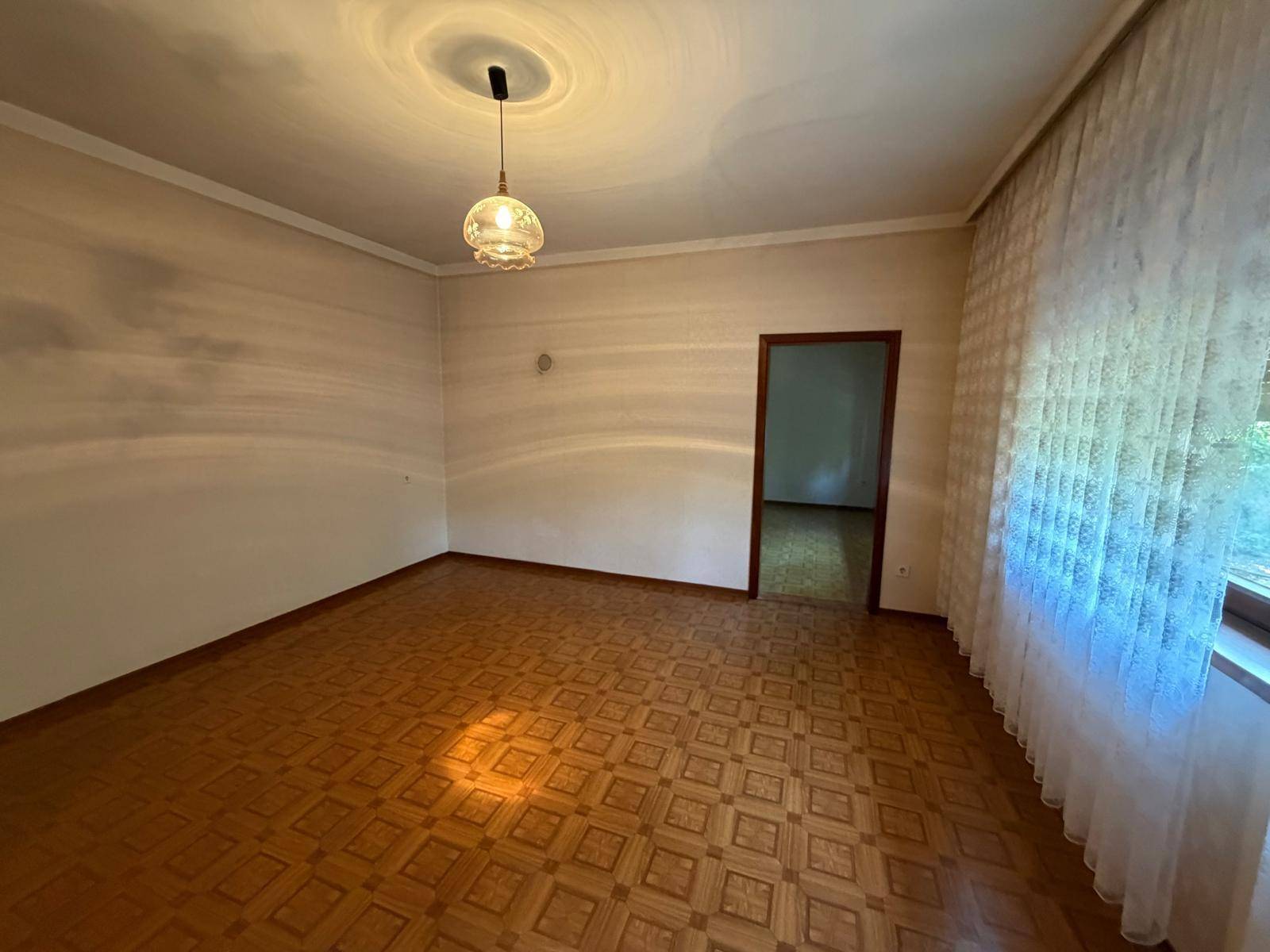 Wohnzimmer mit gemustertem Linoleumboden, weißer Decke und Zugang zu einem weiteren Raum.