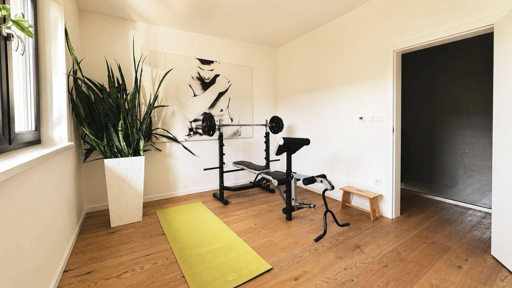 Heller Fitnessraum mit Trainingsbank, Yogamatte und großem Fenster für natürliches Licht.