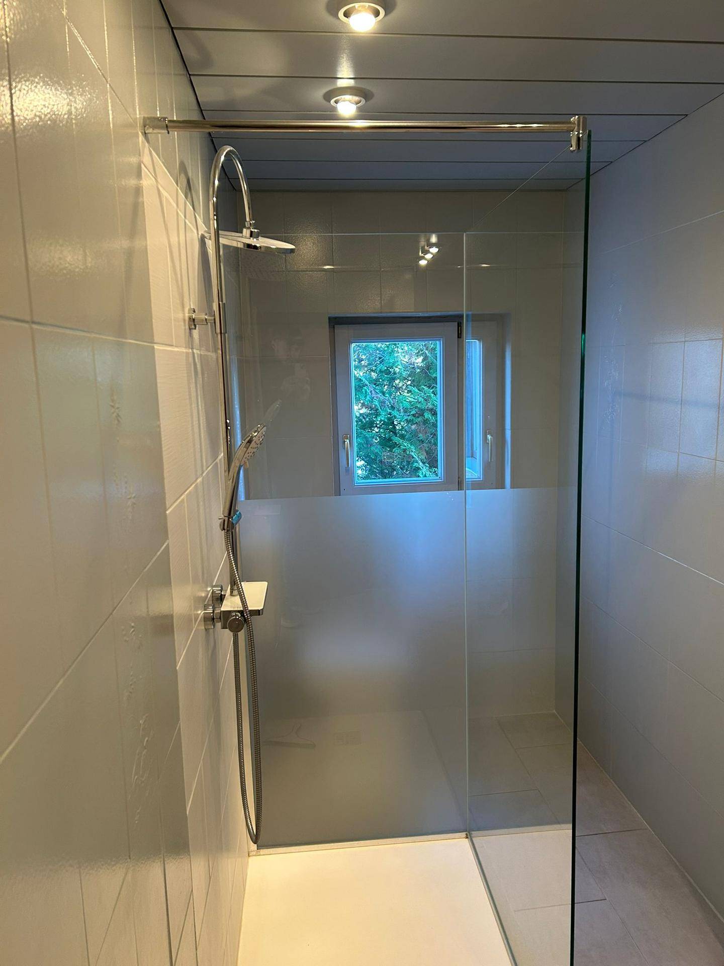 Modernes Badezimmer mit begehbarer Dusche, weißen Fliesen und Fenster.