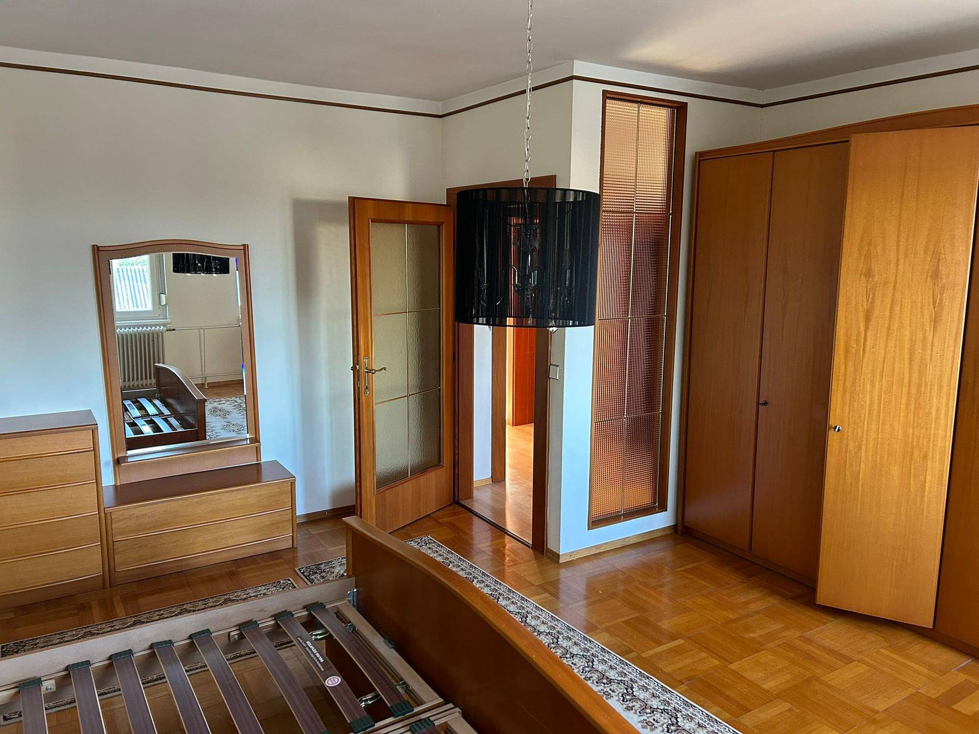 Schlafzimmer mit Holzparkett, passenden Holzmöbeln und einem modernen Deckenlicht.