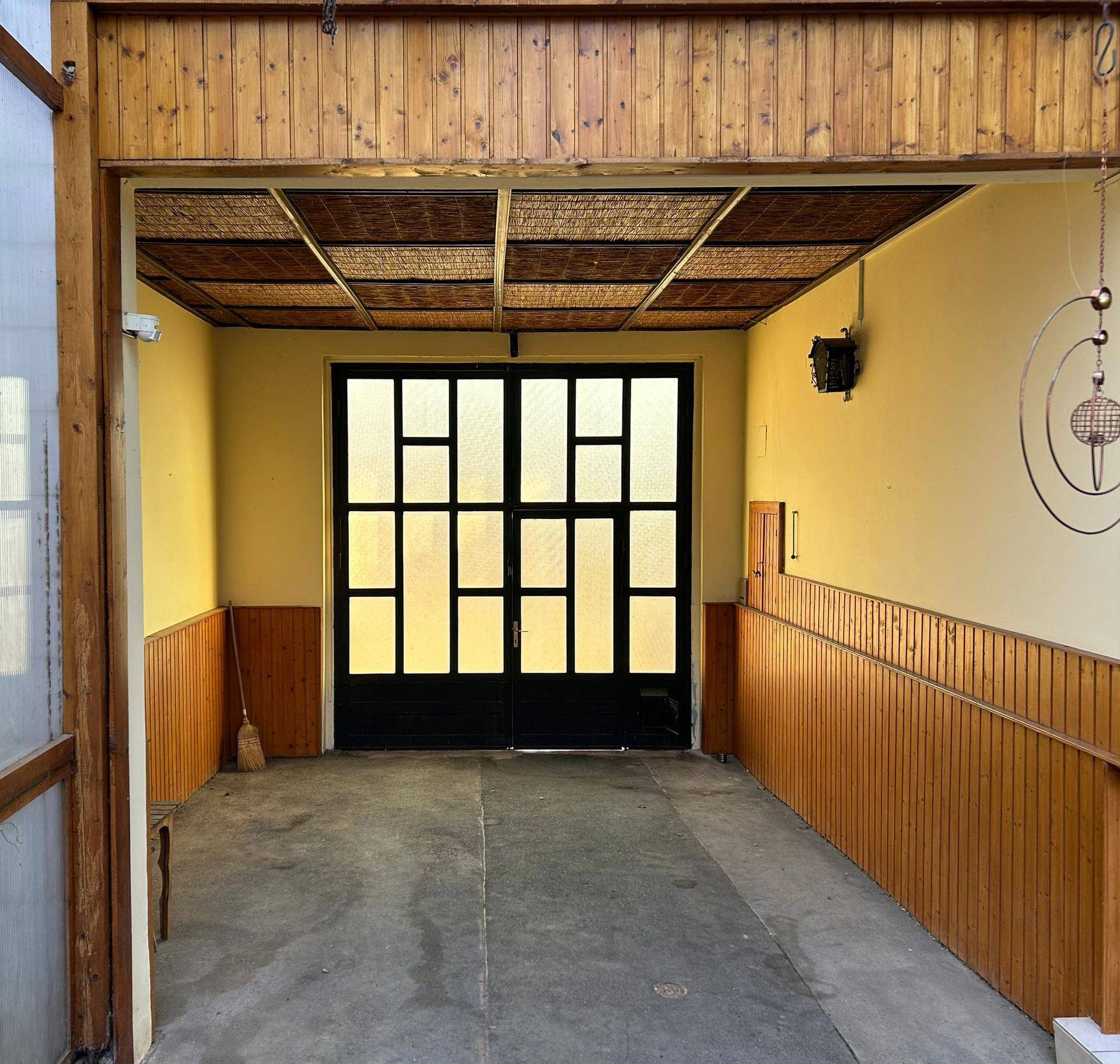Geräumige Garage mit Holzwänden, Betonboden und großem Tor mit Glasfenstern.