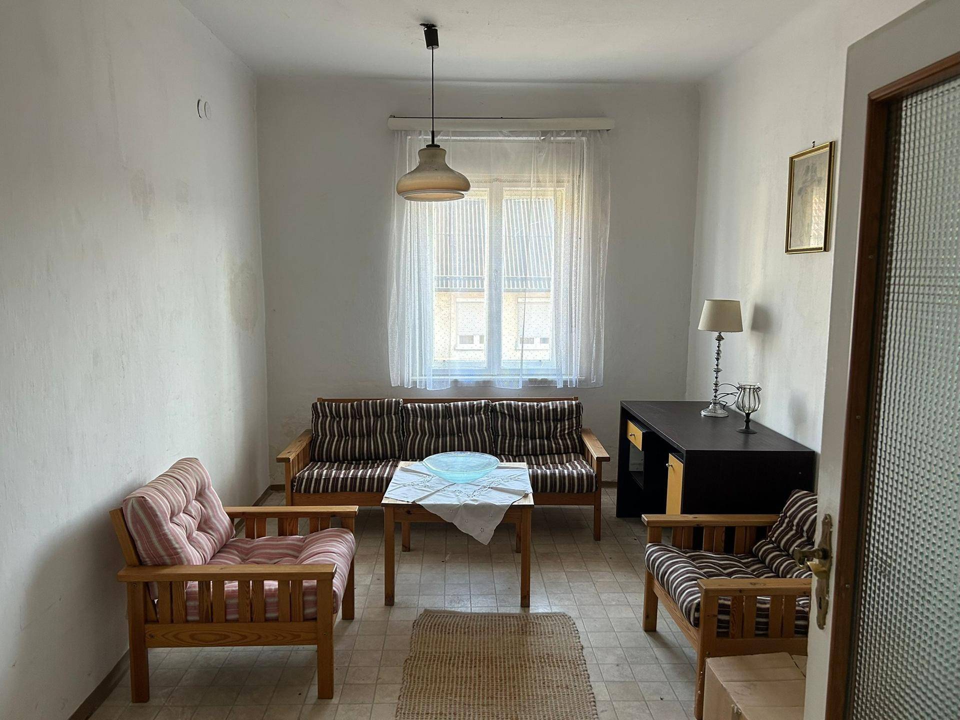 Wohnzimmer mit Vintage-Möbeln, Teppichboden und Fenster mit hellen Vorhängen.