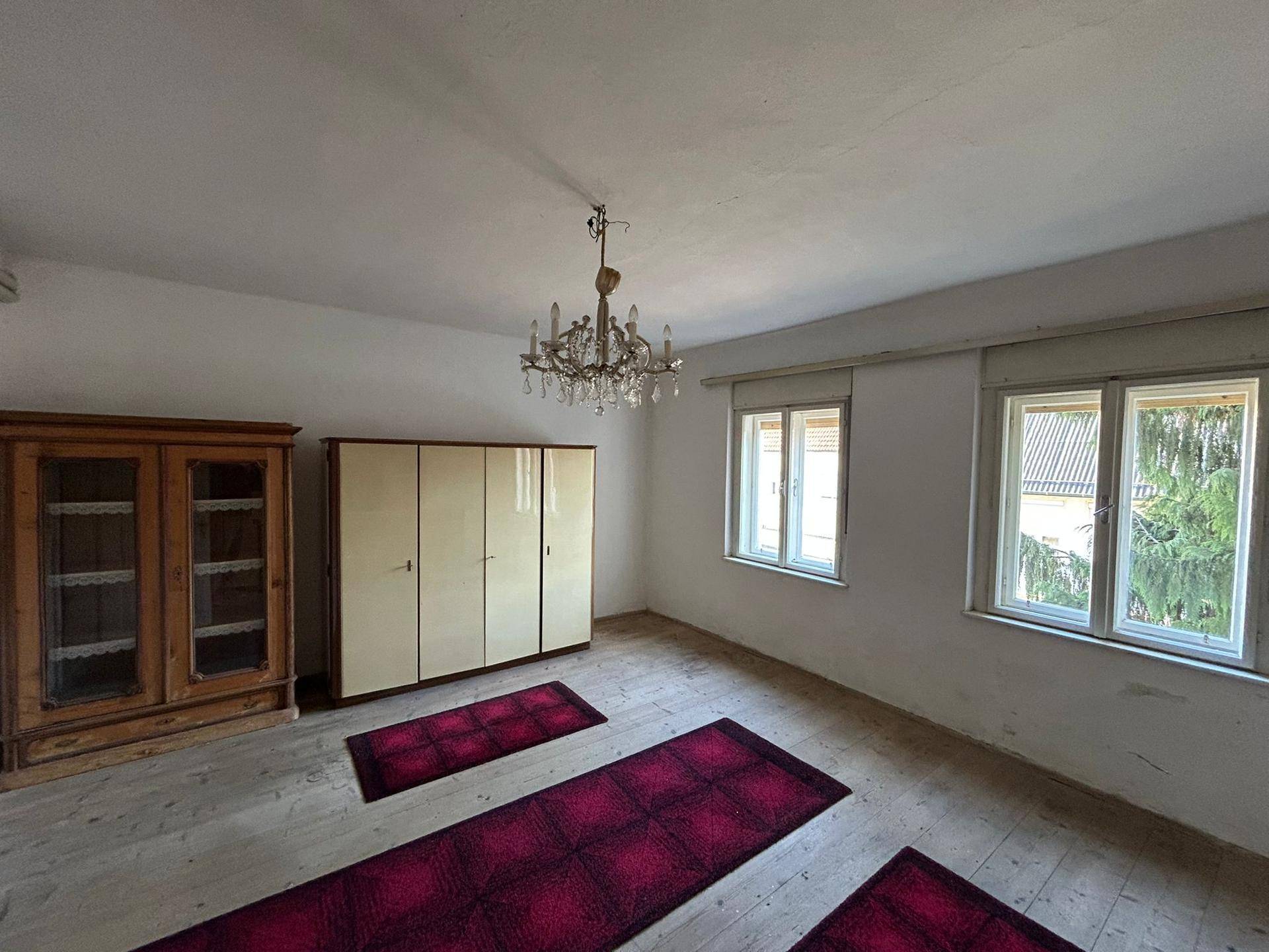 Schlafzimmer mit Holzboden, antiken Möbeln und Kronleuchter, bereit zur Renovierung.