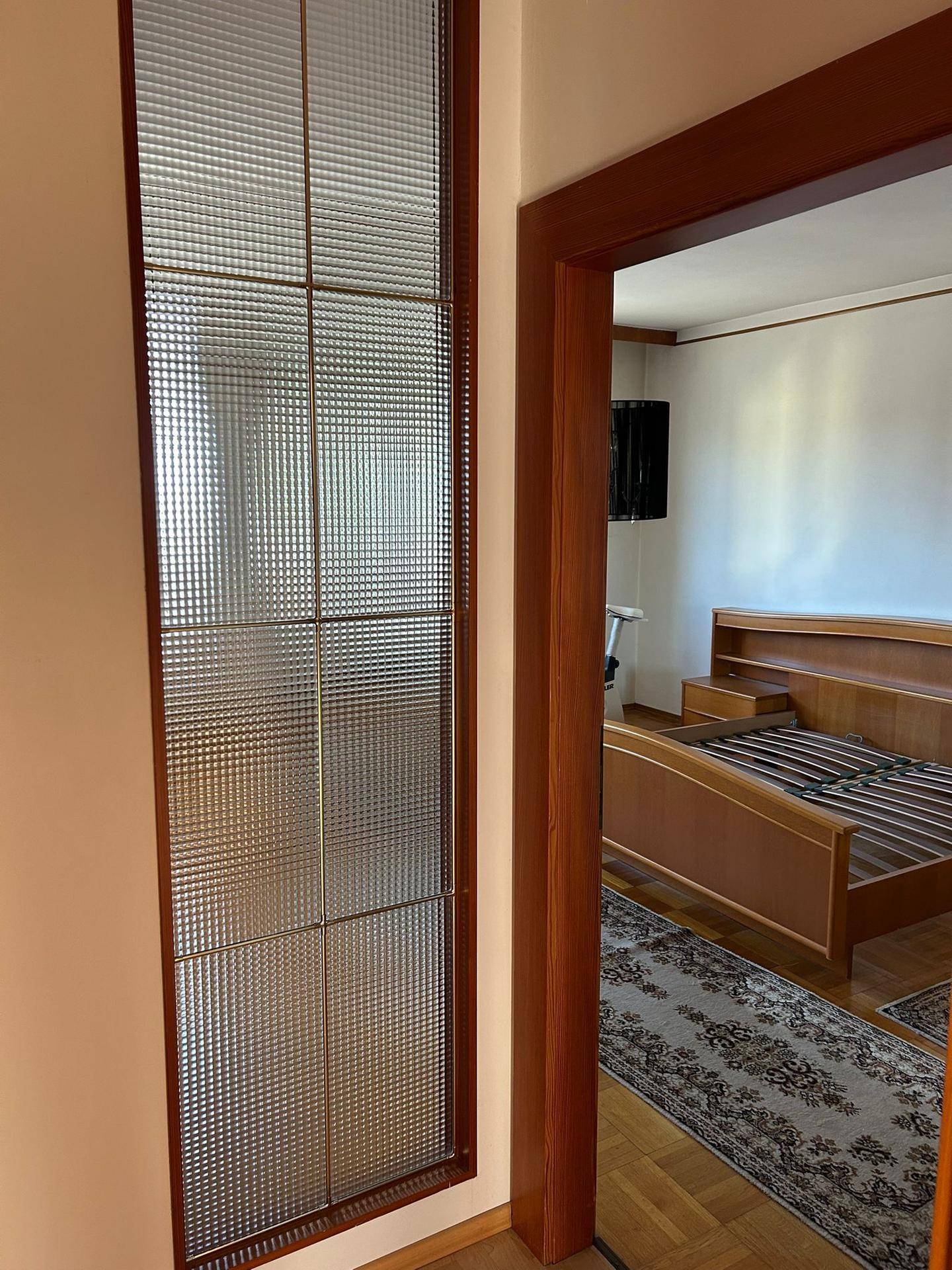 Flur mit Holztür und strukturiertem Glasfenster, das zu einem Schlafzimmer führt.
