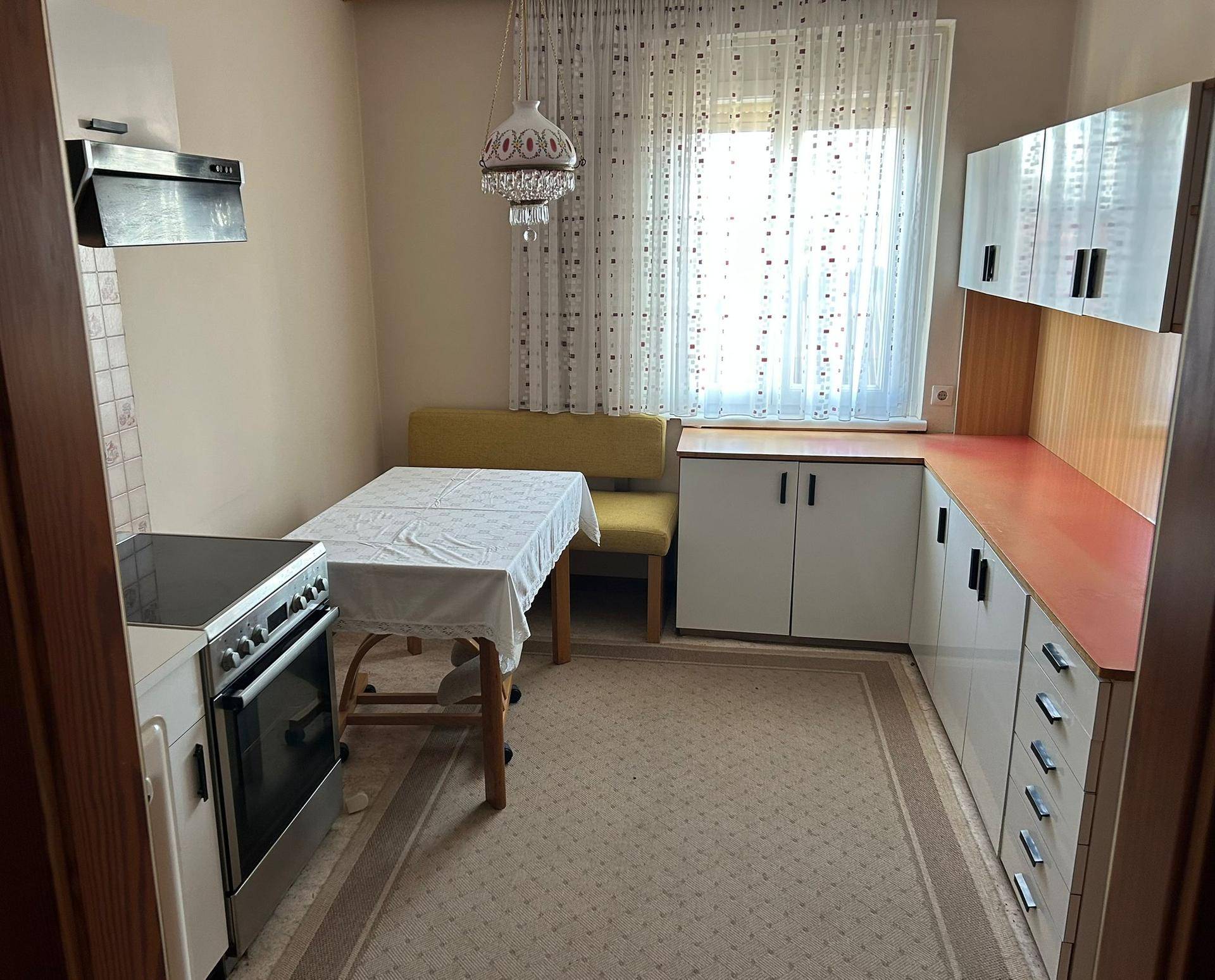 Gemütliche Wohnküche mit Esstisch, Einbauschränken und Fenster mit Vorhängen.