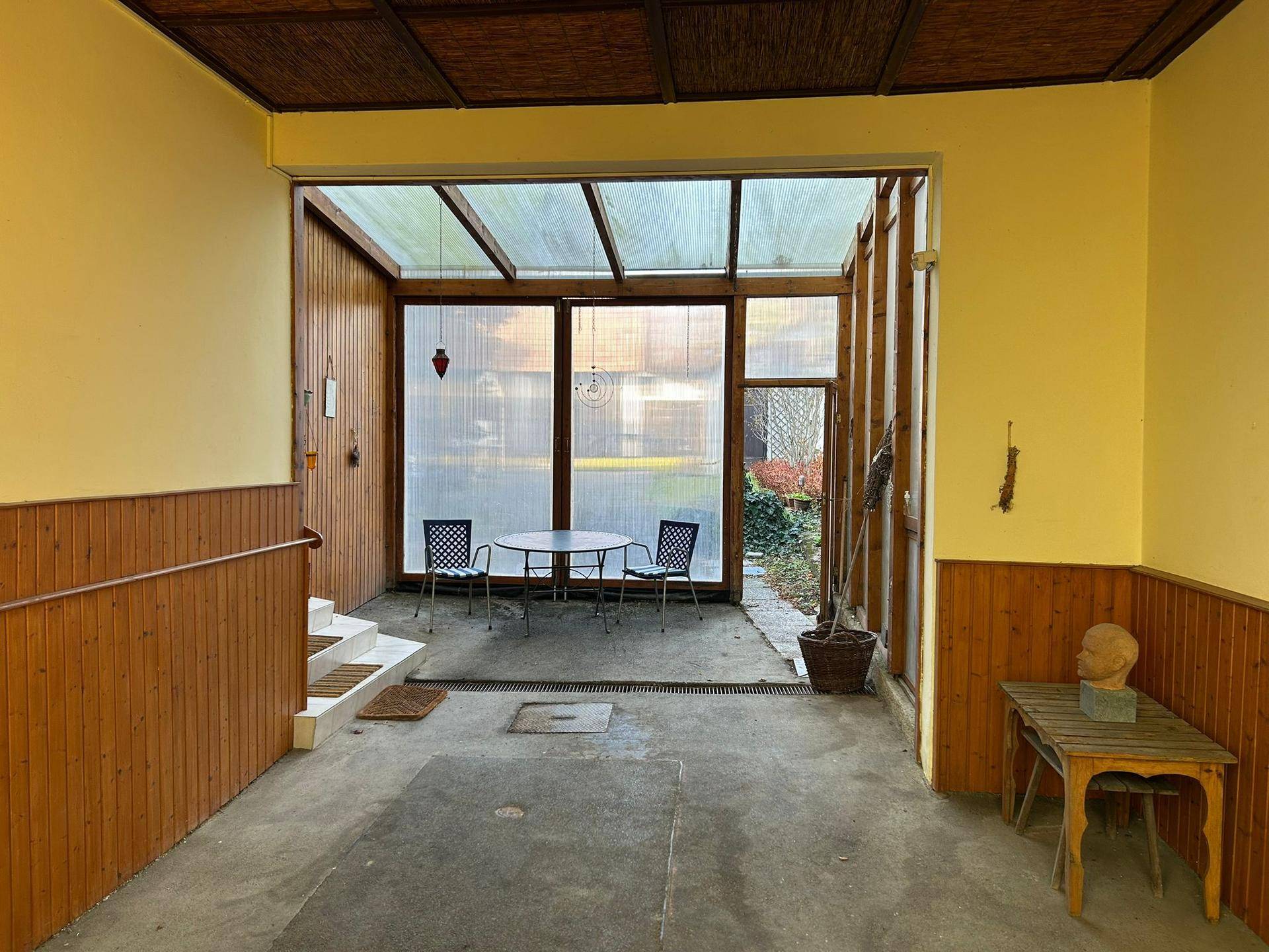 Heller Wintergarten mit Sitzgelegenheiten, Holzverkleidung und Blick ins Grüne.