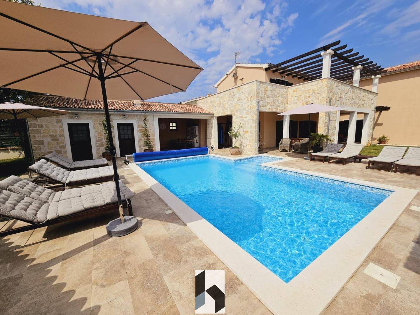 Sonniger Außenbereich der Villa mit großem Pool, Liegestühlen und Sonnenschirmen.