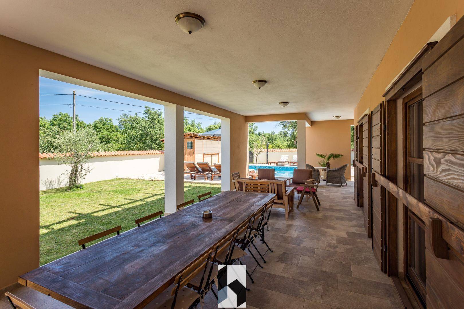 Überdachte Terrasse mit großem Esstisch und Blick auf den Garten und den Poolbereich.
