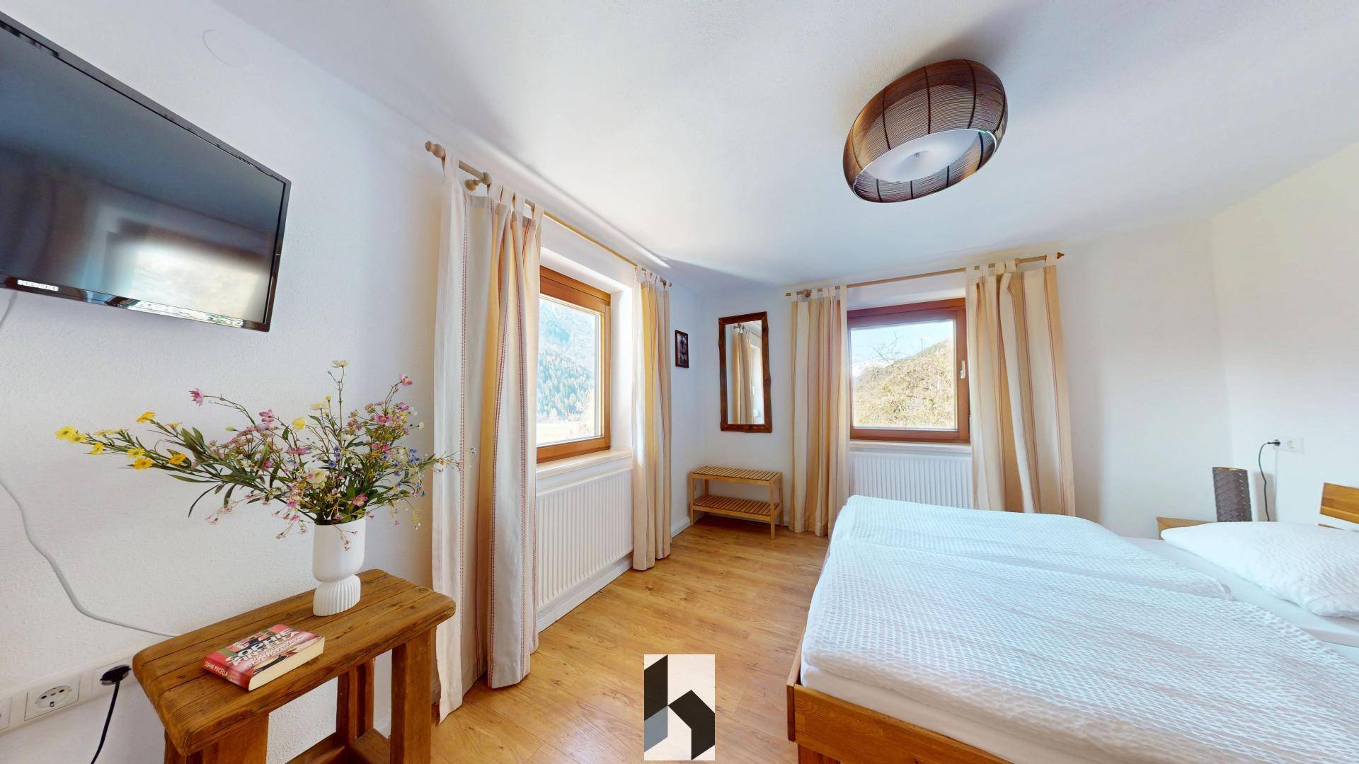 Helles Schlafzimmer mit Doppelbett, Holzboden und Fenstern mit Blick auf die Natur und viel Tageslicht.