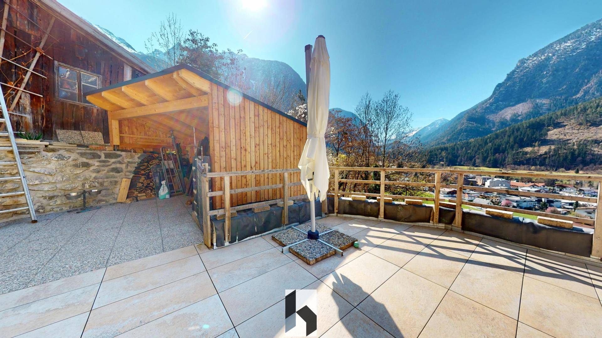 Große geflieste Terrasse mit Sonnenschirm und atemberaubendem Bergblick, ideal für sonnige Tage.