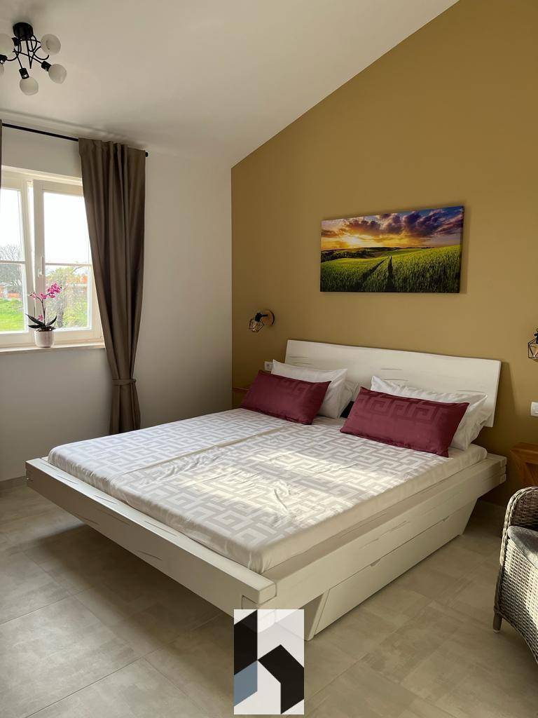 Helles Schlafzimmer mit Doppelbett, gelber Akzentwand und Fliesenboden.
