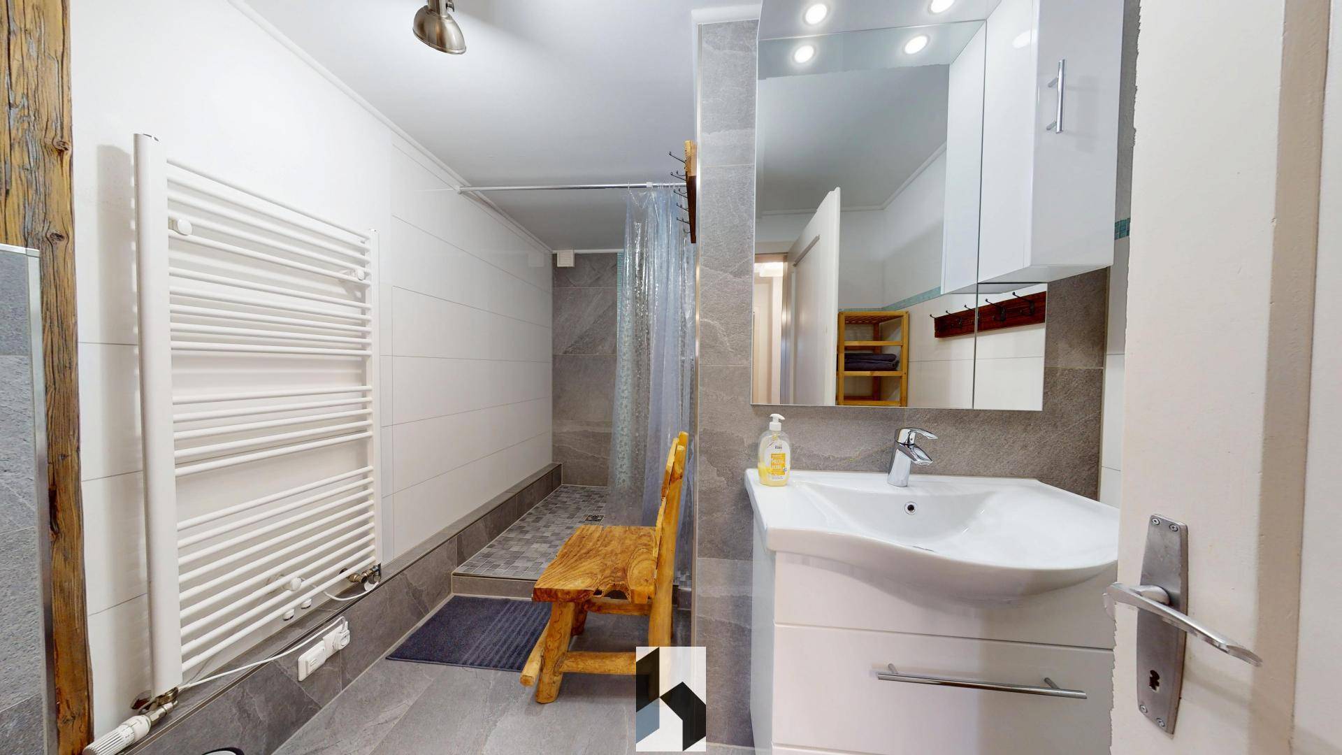 Modernes Badezimmer mit Dusche, Einzelwaschbecken und beheiztem Handtuchhalter in hellen Grautönen.