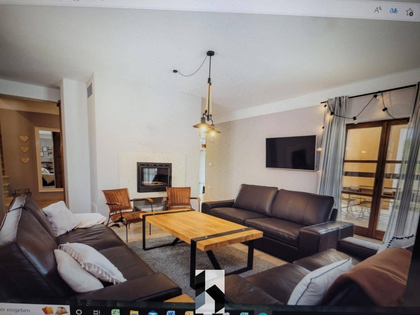 Gemütliches Wohnzimmer mit dunklen Ledersofas, Kamin und Zugang zur Terrasse.