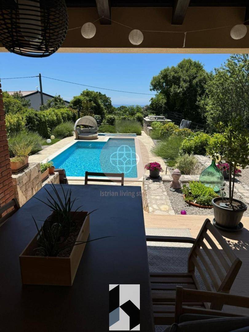 Überdachte Terrasse mit Esstisch, Gartenblick und Pool im Hintergrund.