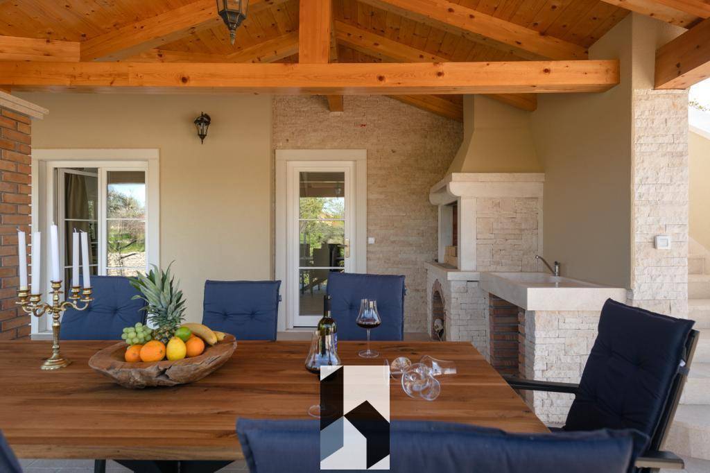 Überdachte Terrasse mit großem Esstisch, Holzbalken und integriertem Grillbereich.