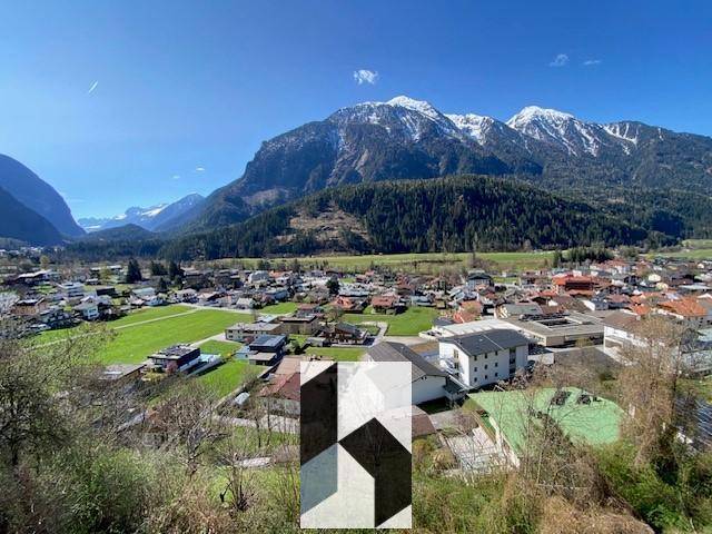 Weitläufiger Blick auf ein malerisches Dorf und die umliegende Berglandschaft unter blauem Himmel.