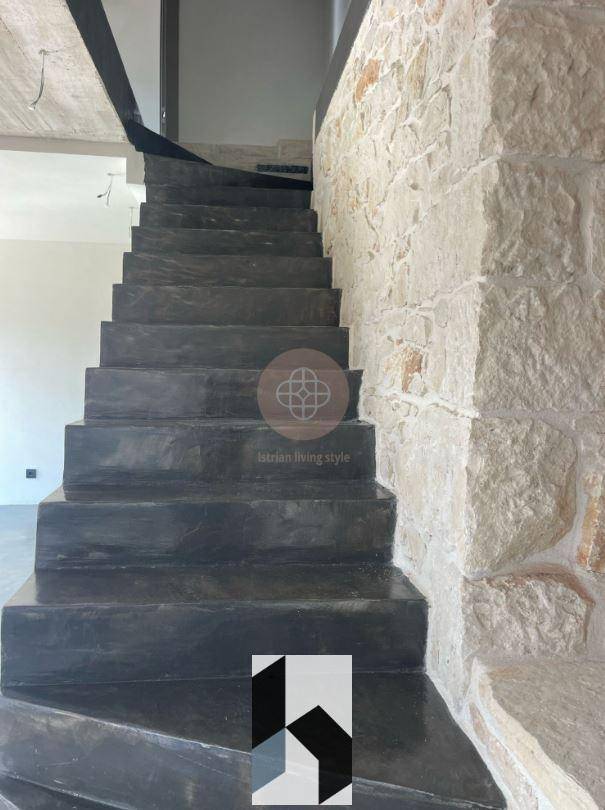 Dunkle Betontreppe neben einer rustikalen Steinwand in einem noch unfertigen Innenbereich.