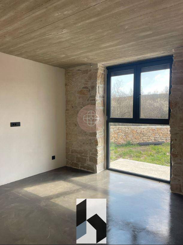 Unmöblierter Raum mit großer Fensterfront, Steinwand und Betonboden, bietet viel Tageslicht.