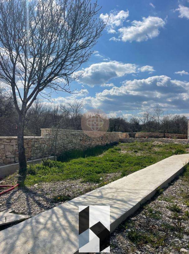 Unentwickelter Gartenbereich mit Steinmauern und einem Betonweg, umgeben von Natur.