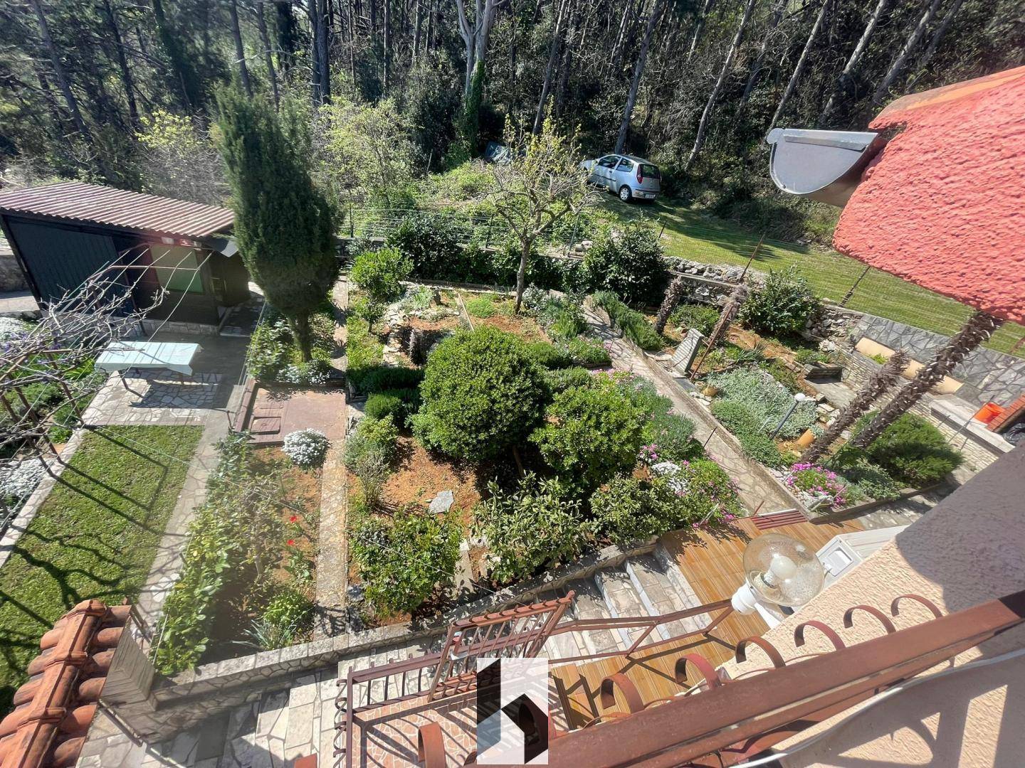 Terrassierter Garten mit Treppen und üppiger Bepflanzung, umgeben von Wald.